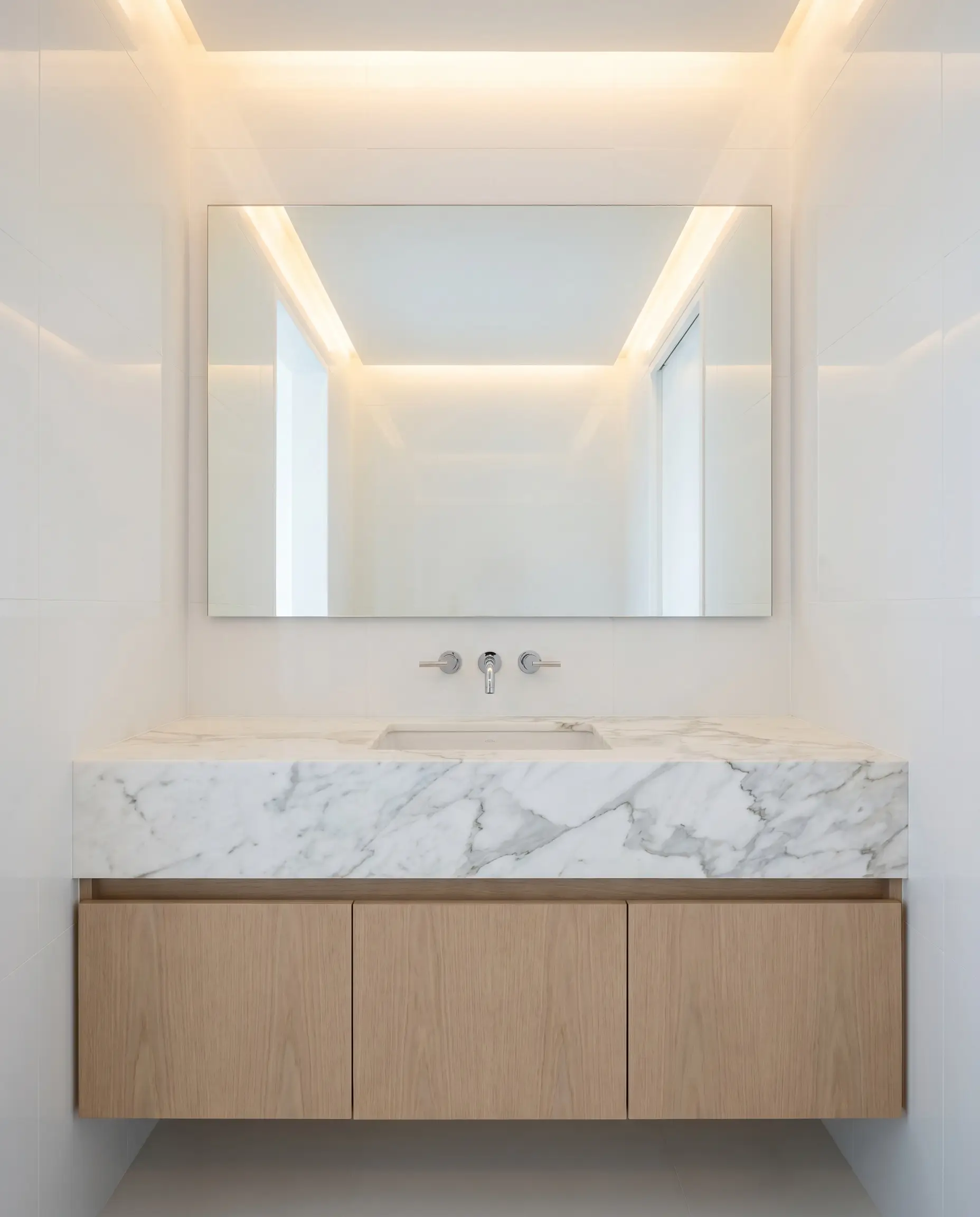 A thick five-inch mitered edge profile creates a monolithic calacatta statuario marble countertop resting seamlessly on minimalist flat-panel white oak cabinetry.
