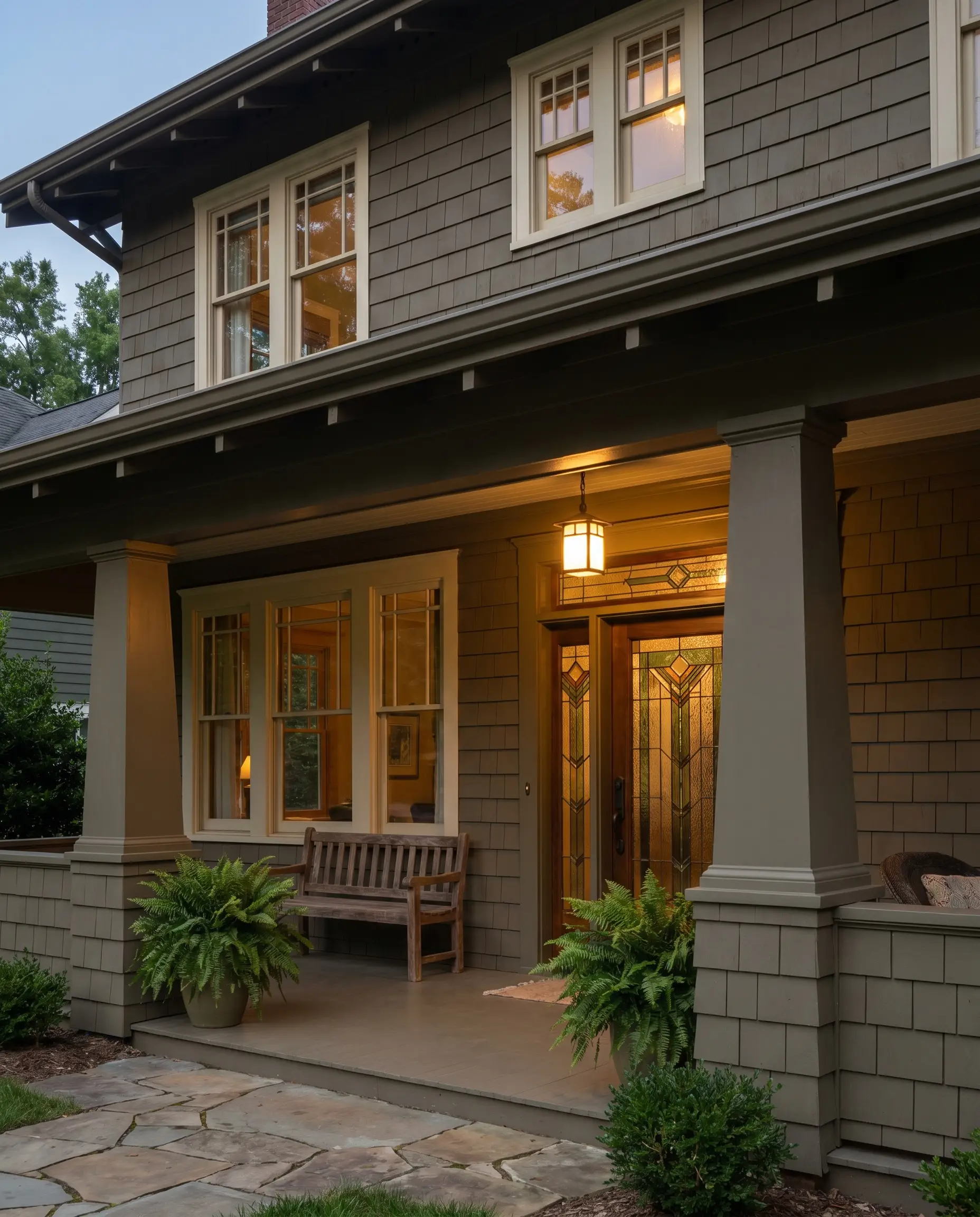 Deep olive-gray siding and tapered columns surround a beautiful Craftsman-style stained glass entry door and intricate window mullions painted in deep cream.