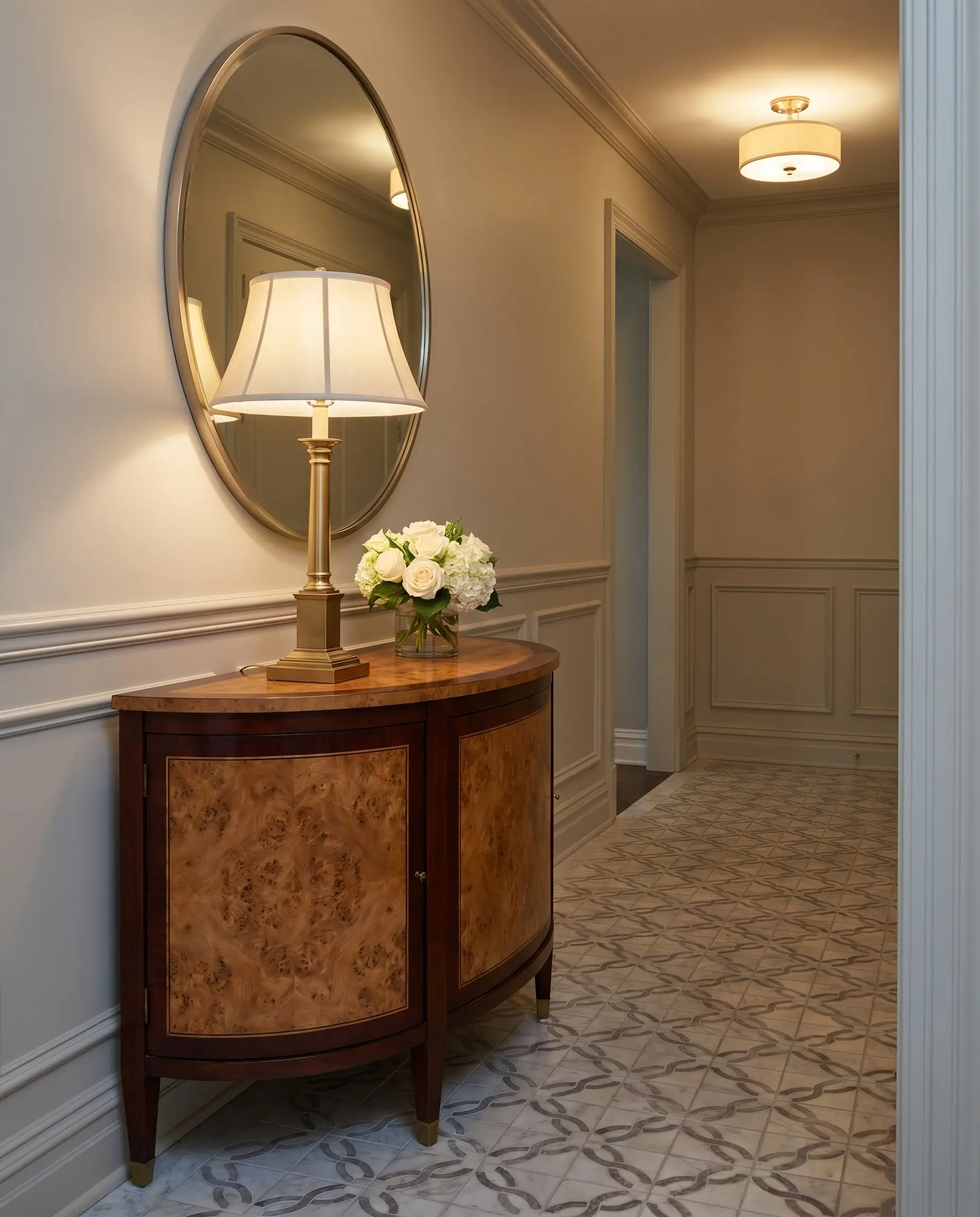 A half-moon demilune console table featuring a highly active burl wood inlay and dark mahogany border softens the rigid architecture of a transitional foyer.