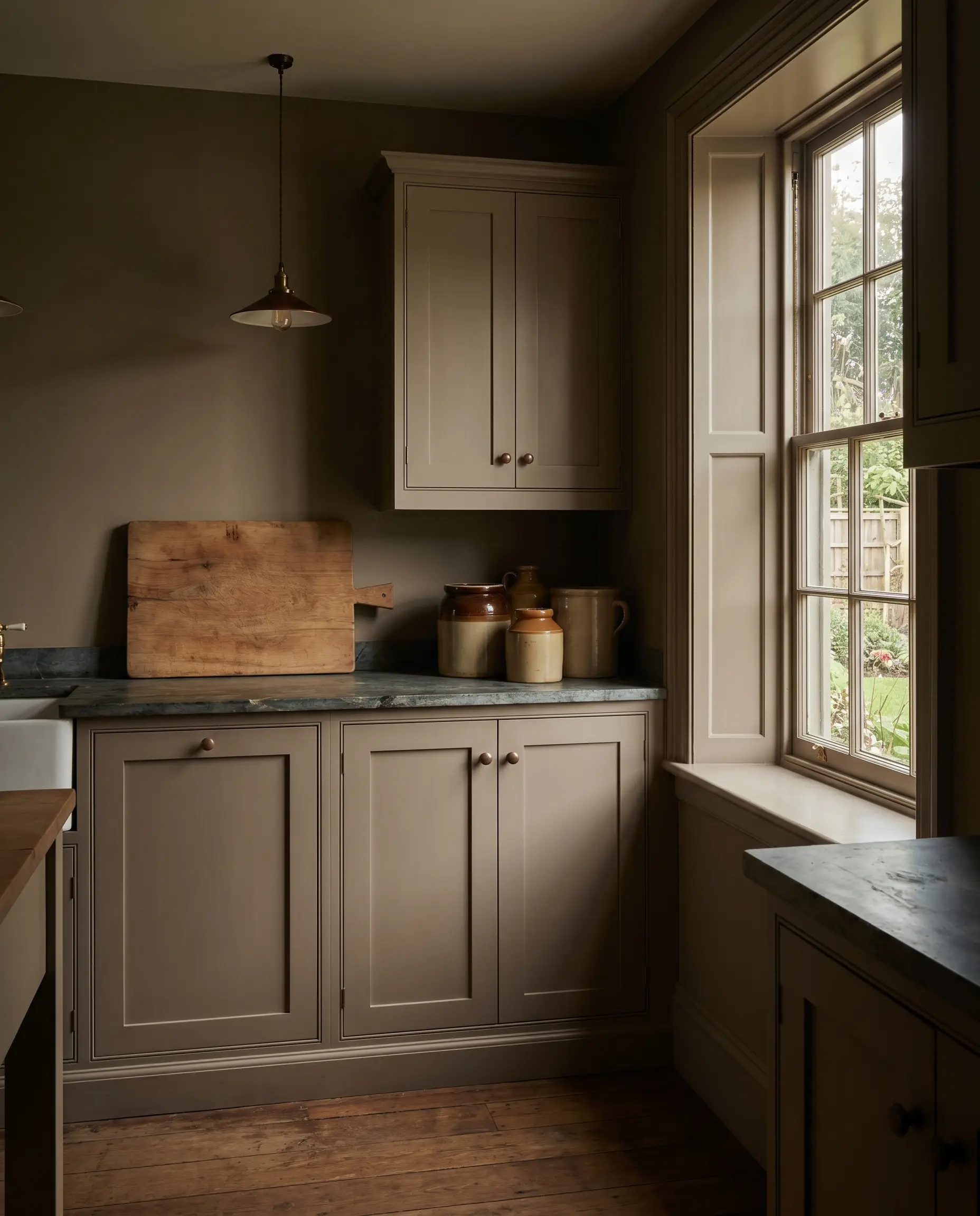 Custom inset English Shaker cabinetry painted in Farrow and Ball Drop Cloth features matching baseboards, window trim, and styled vintage ceramic crocks.