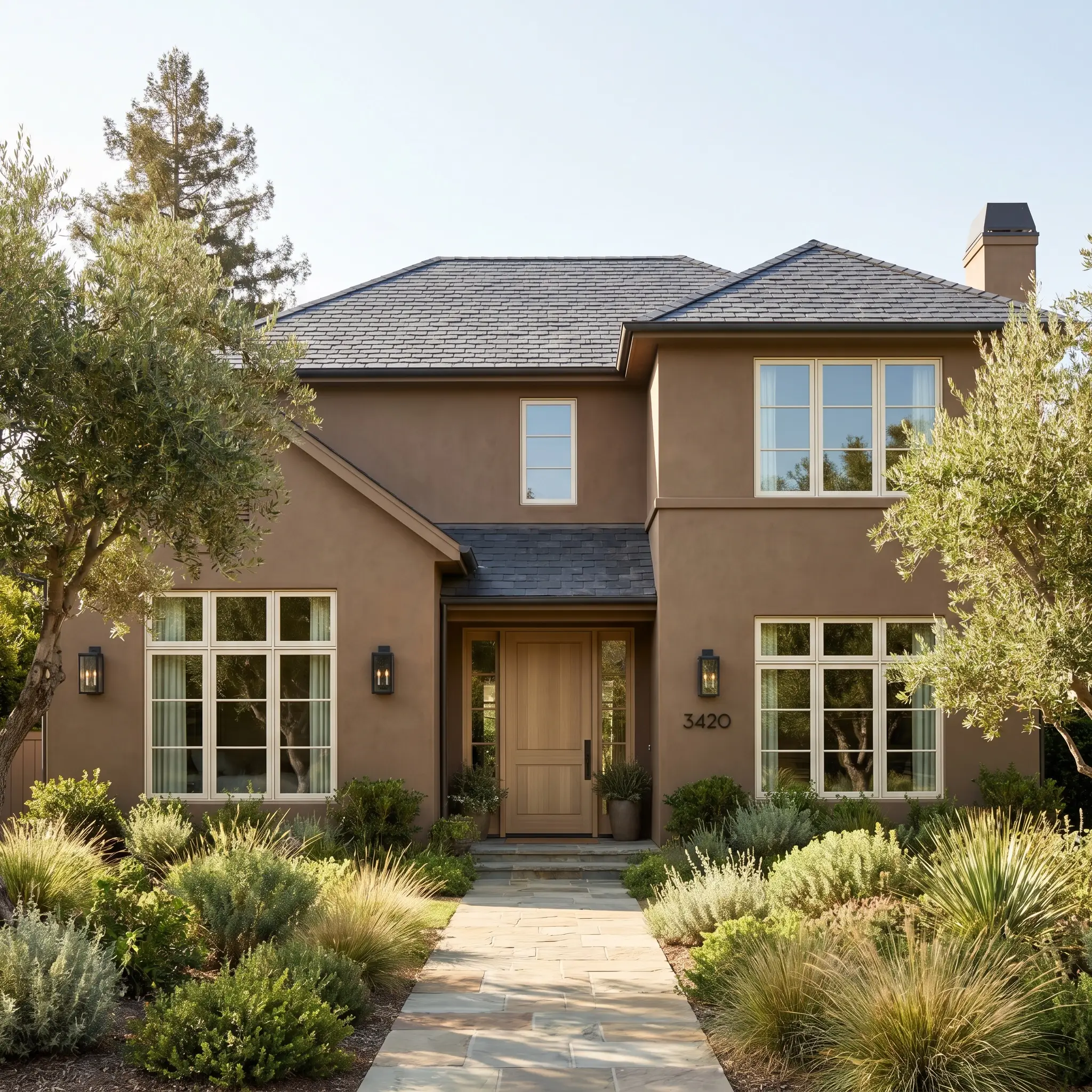 Crisp warm-white trim and a natural slate roof frame smooth earthy cast stucco walls, blackened steel sconces, and a solid pale oak front door.