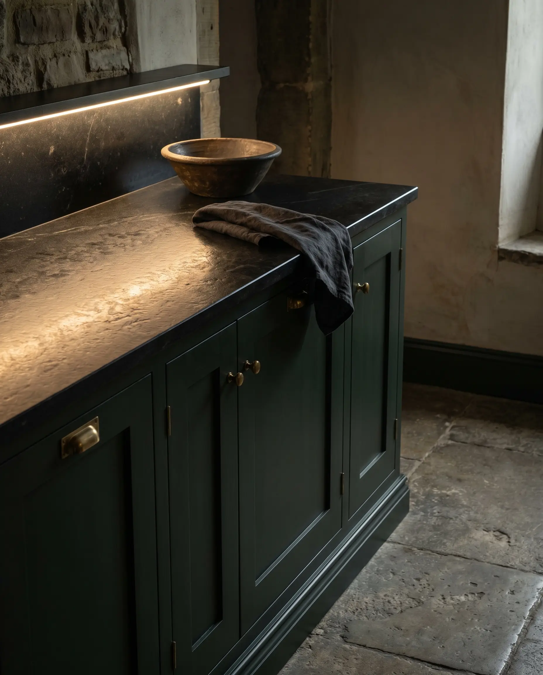 Custom base cabinetry painted in Benjamin Moore Essex Green supports a pitch-black oiled soapstone countertop styled with a vintage ironstone bowl and dark linen towel.