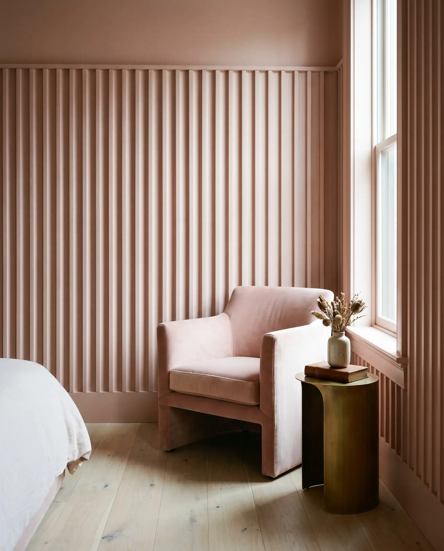 Floor-to-ceiling fluted white oak wainscoting in a monochromatic matte blush finish surrounds a plush velvet side chair resting on wide-plank hardwood floors.