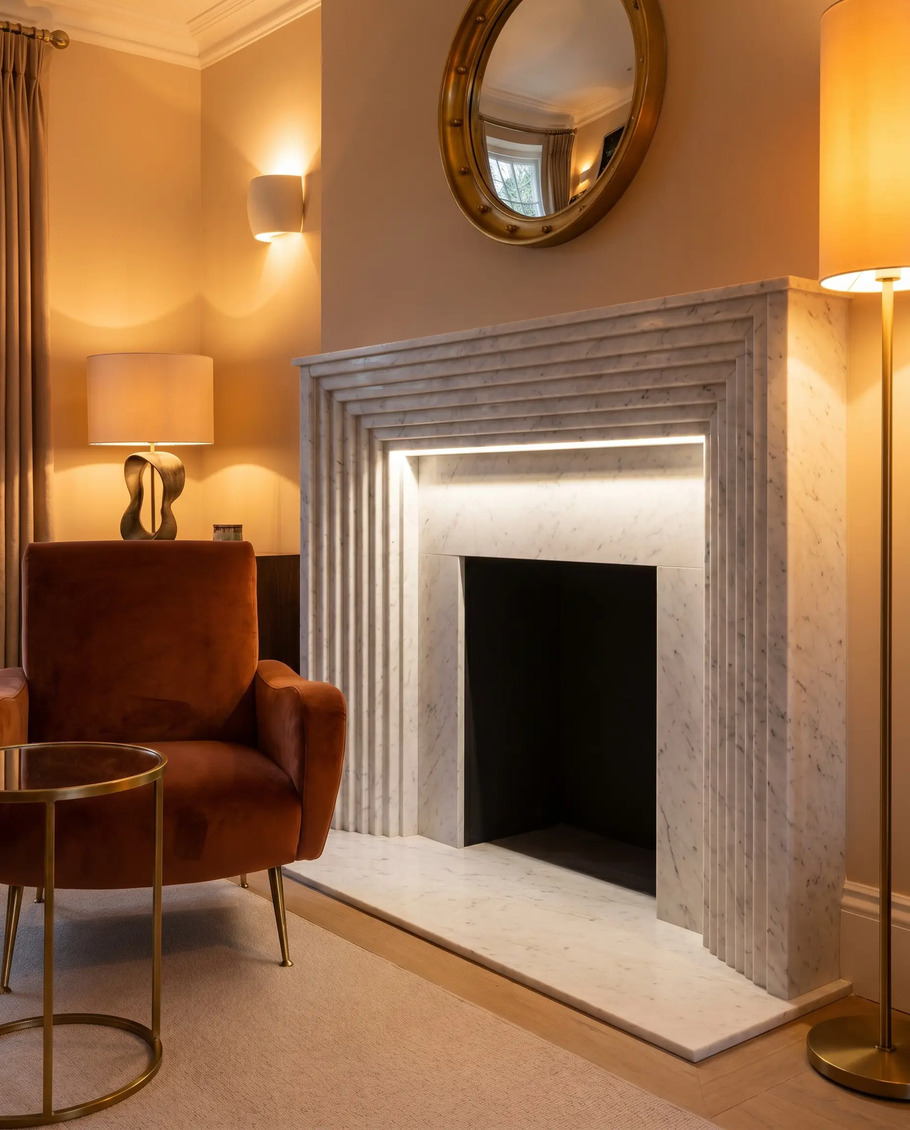 Deep vertical fluted ridges are carved directly into a solid Carrara stone surround resting on a flat un-milled white hearth beside a velvet side chair.