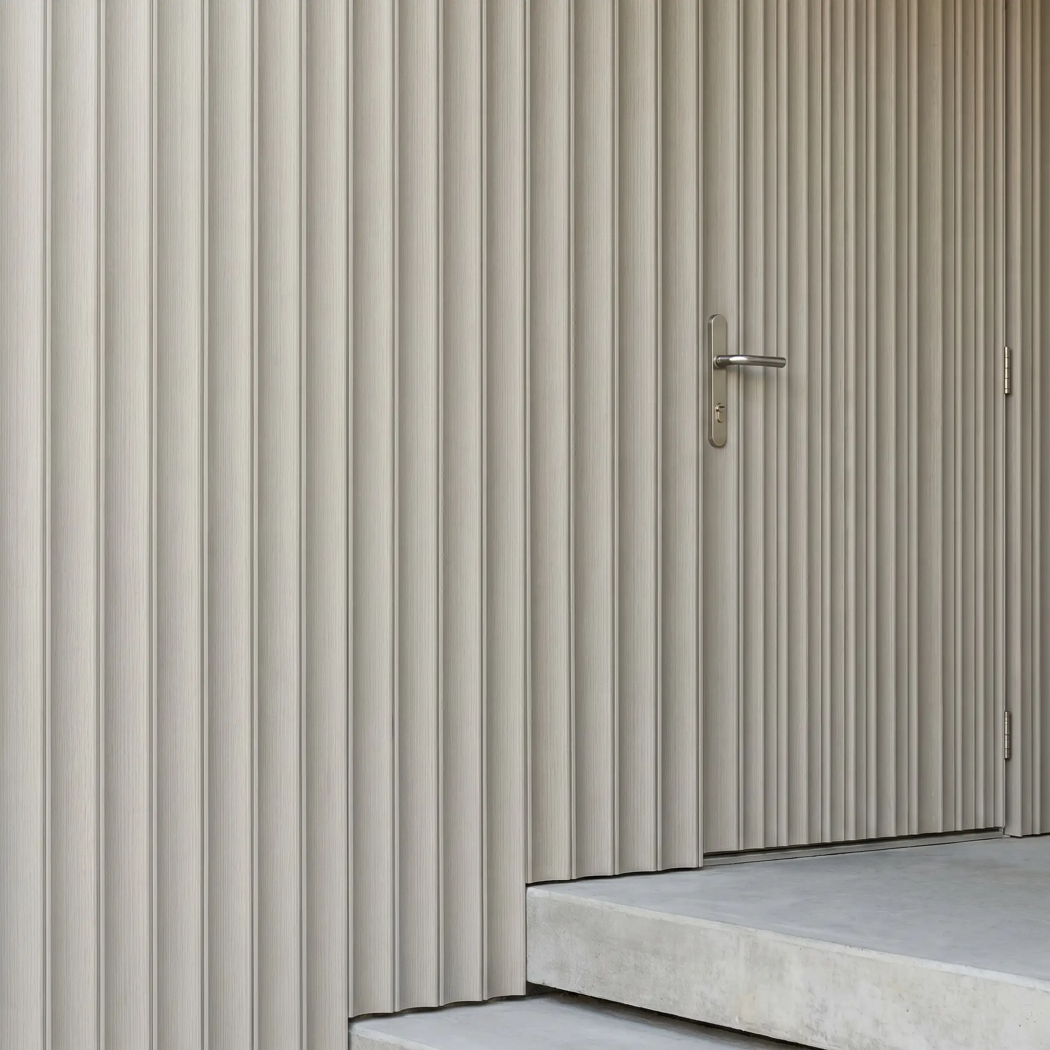 A highly tactile accent wall features fluted exterior composite cladding coated in a soft greige, complete with a sleek brushed nickel door handle.