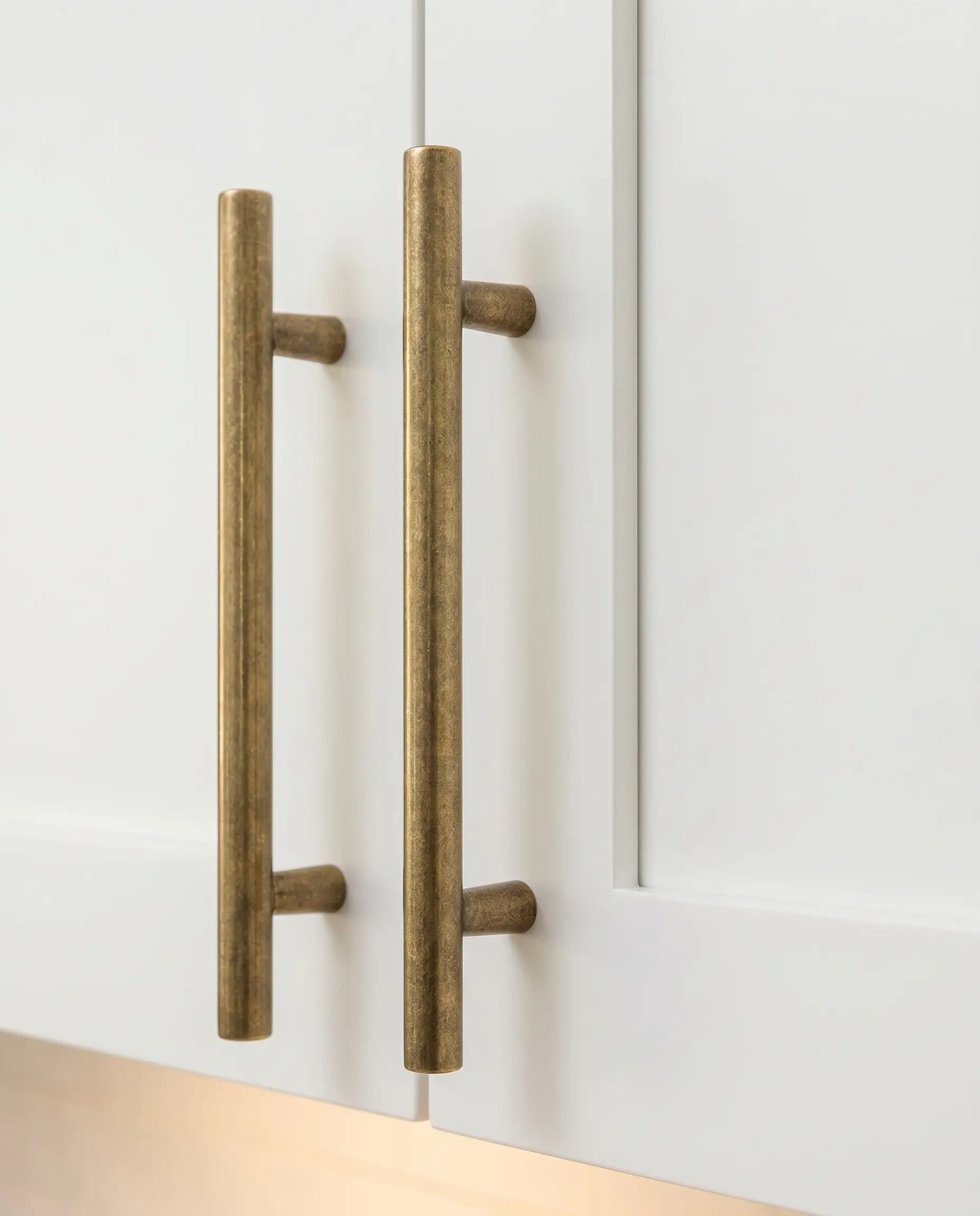 Heavy cast brass T-bar knobs align vertically on crisp white shaker upper cabinet doors above a beautifully styled coffee station.