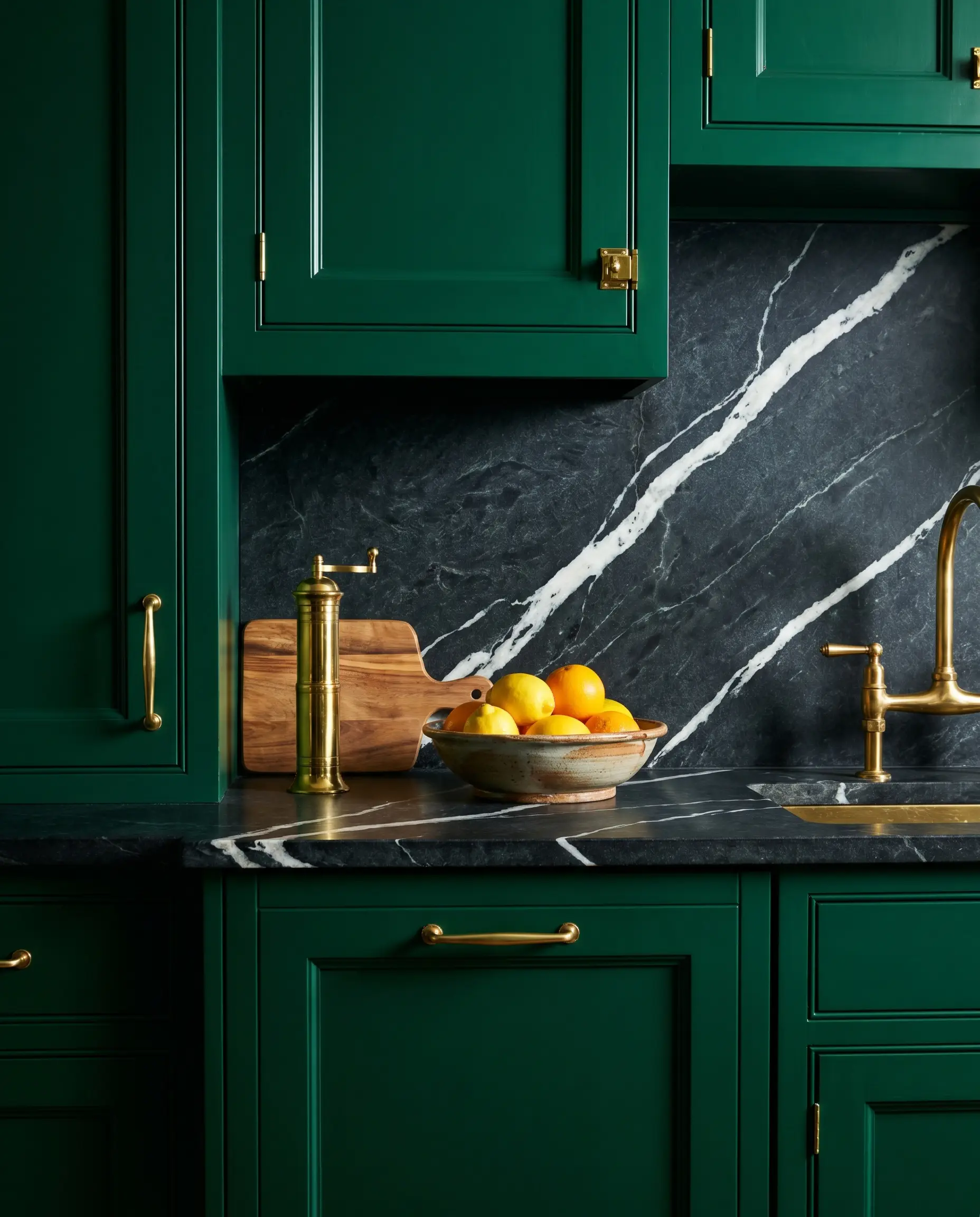 Belvedere steatite soapstone with aggressive white quartz veining sits atop saturated emerald green cabinetry, accented by a sleek brass pepper mill and bright citrus bowl.