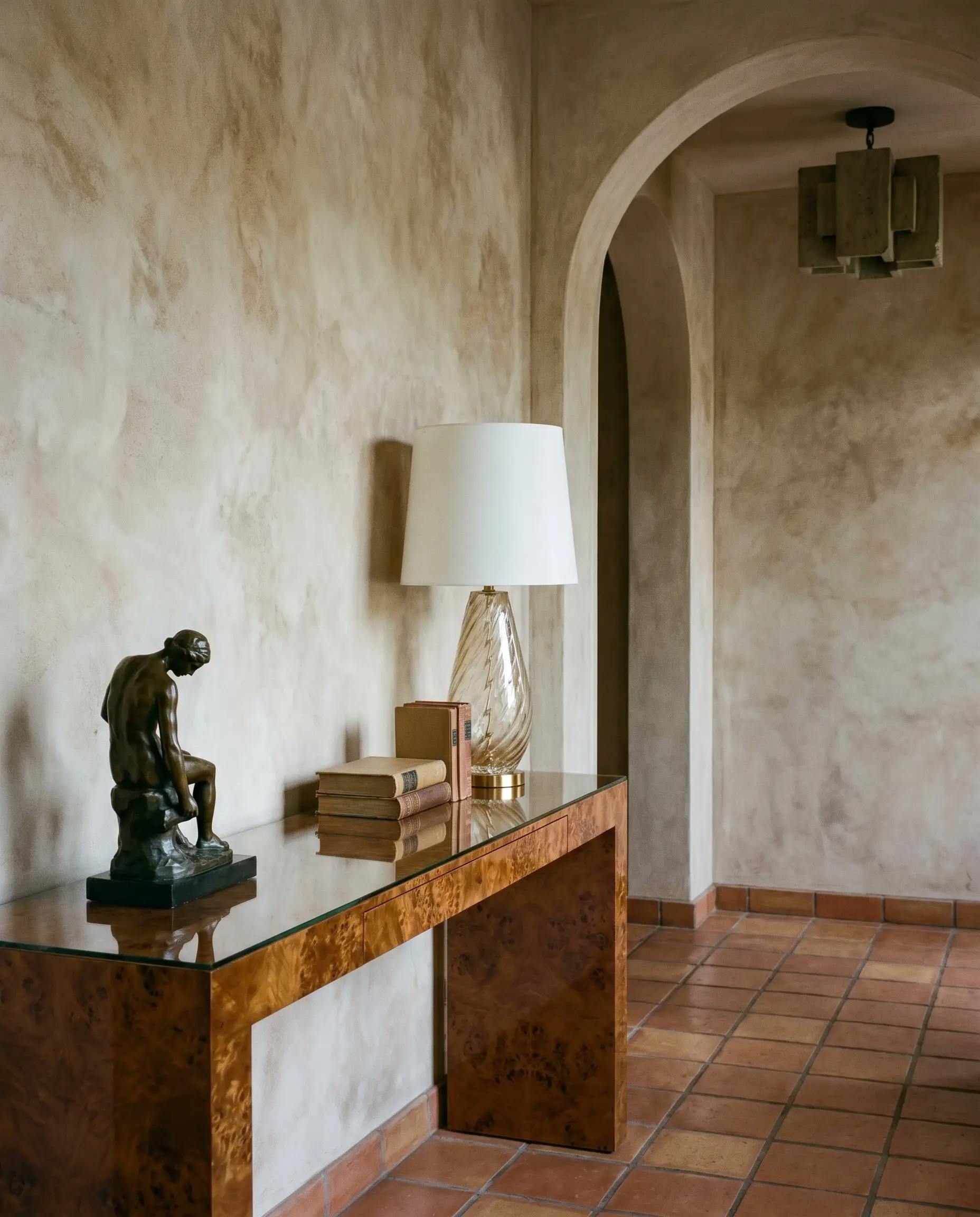 A high-gloss polished burl wood console table displaying a curated vignette creates striking visual tension against dry, chalky Venetian plaster entryway walls.