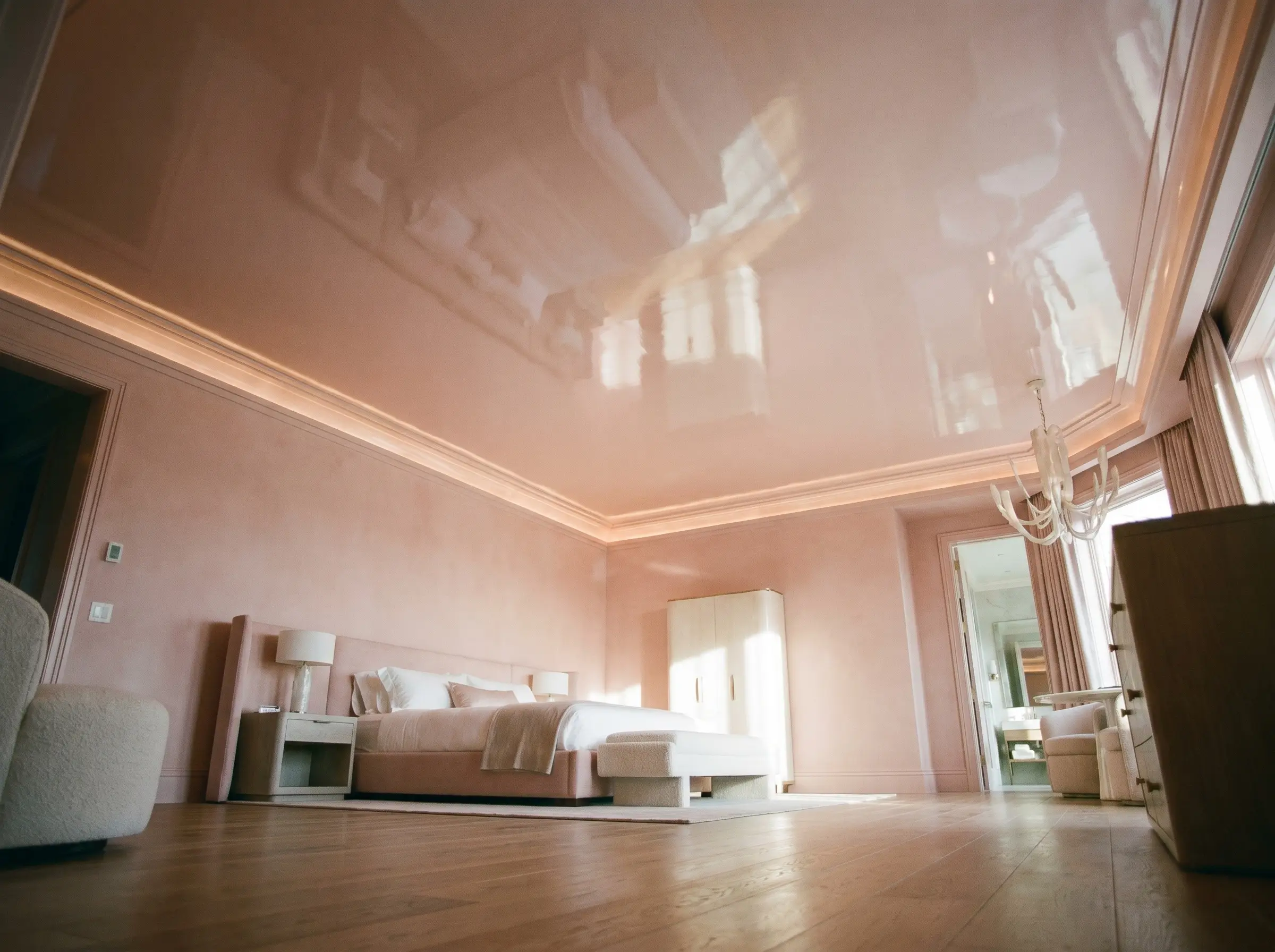 A pale high-gloss pink lacquer ceiling reflects an architectural bed and wide-plank oak floors within a sophisticated luxury pink girl bedroom design.