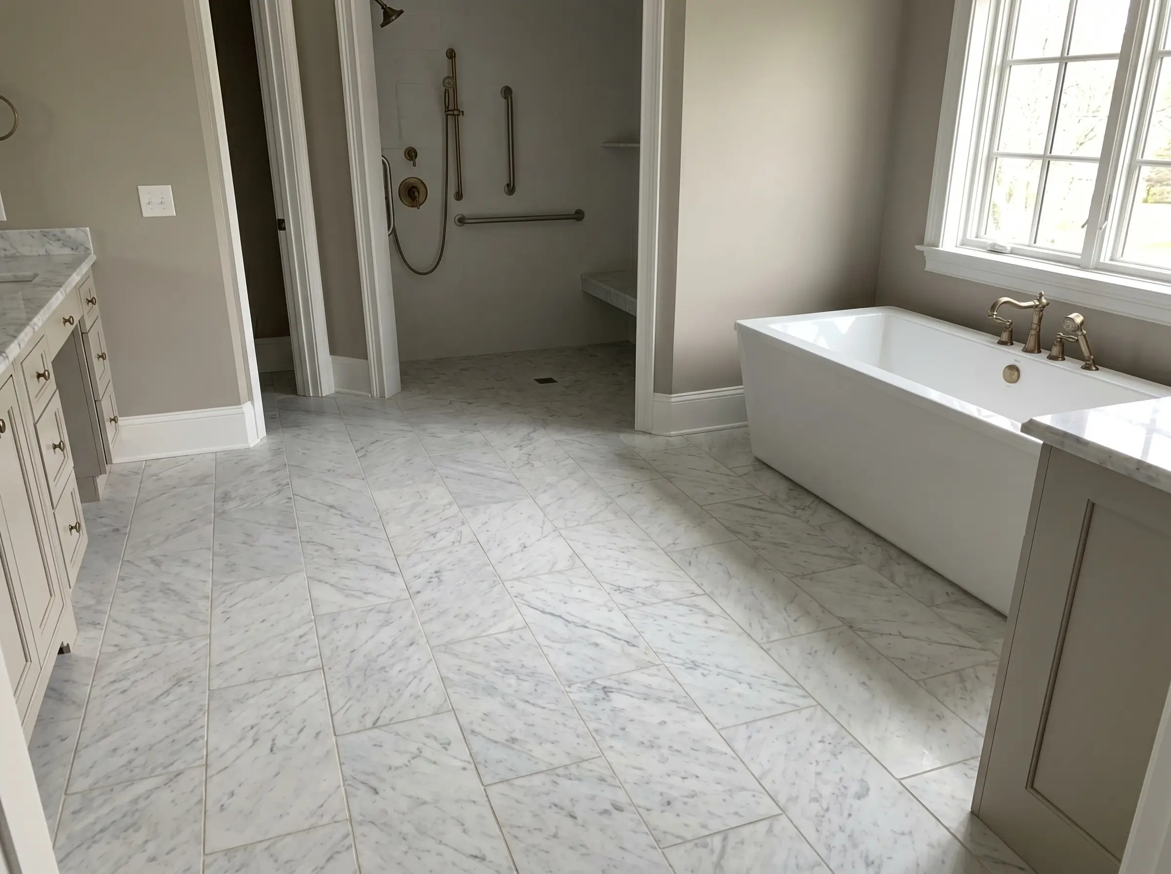 Large honed Carrara marble floor tiles with warm gray grout ground a crisp white freestanding bathtub and subtle baseboards in a spacious washroom.