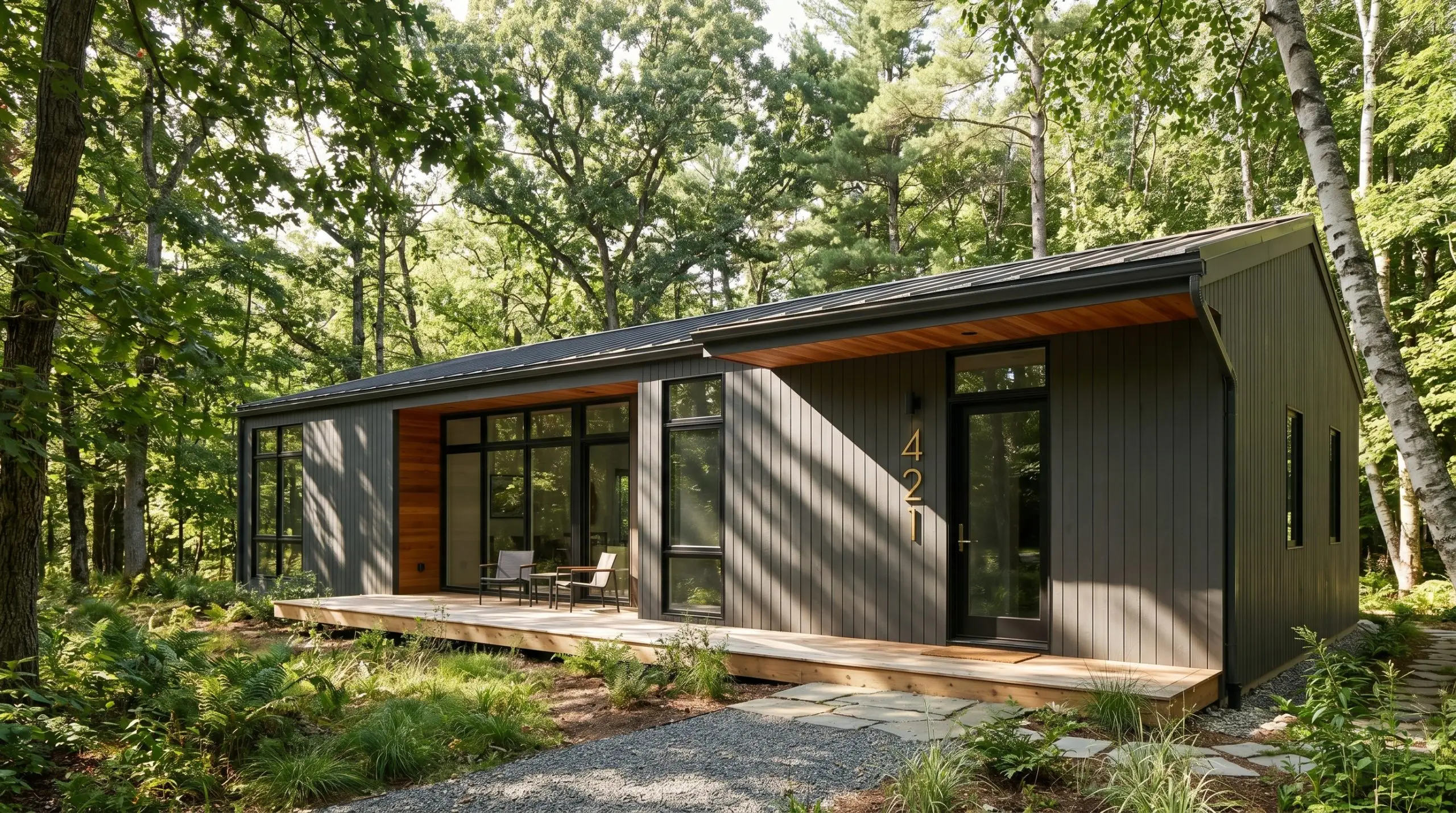 A modern woodland home exterior painted in Benjamin Moore Iron Mountain (Hex #575553) features natural cedar soffits and unlacquered brass house numbers.