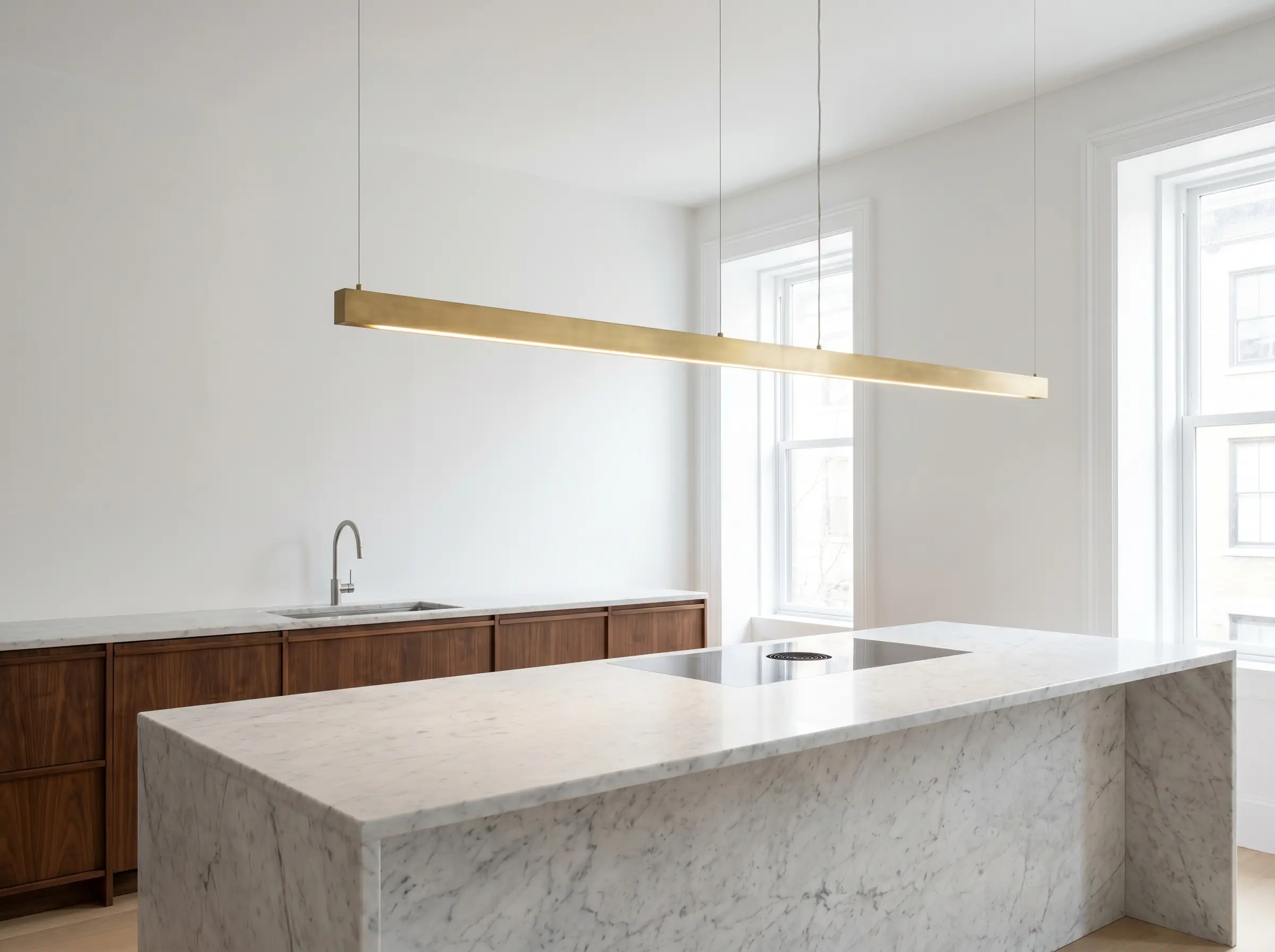 A sleek unlacquered brass linear suspension bar provides statement lighting for low ceilings over a modern kitchen island with warm walnut lower cabinets.