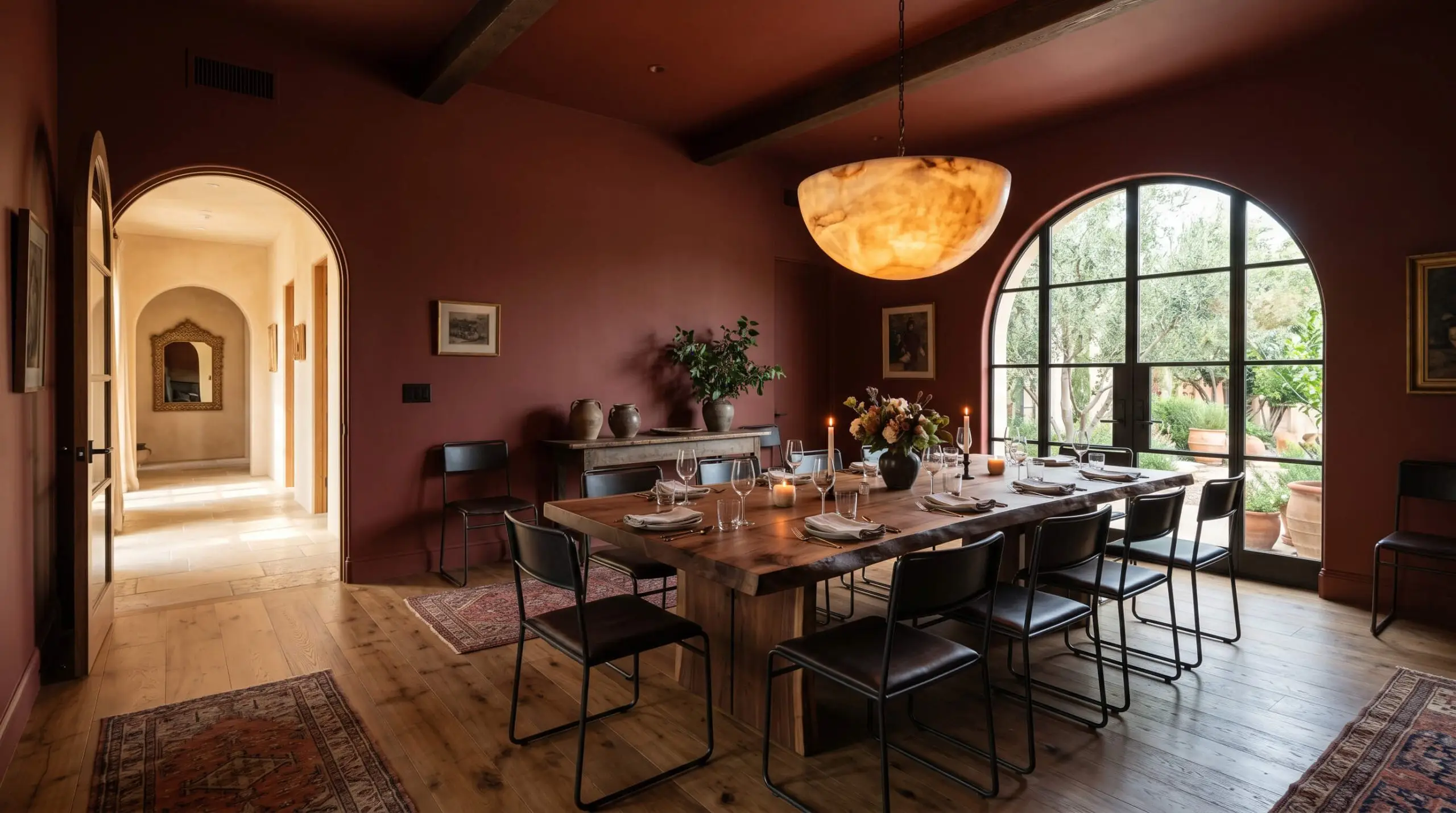A raw live-edge wooden dining table and sleek blackened steel chairs sit beneath an oversized alabaster pendant light enveloped by an earthy orange architectural finish.