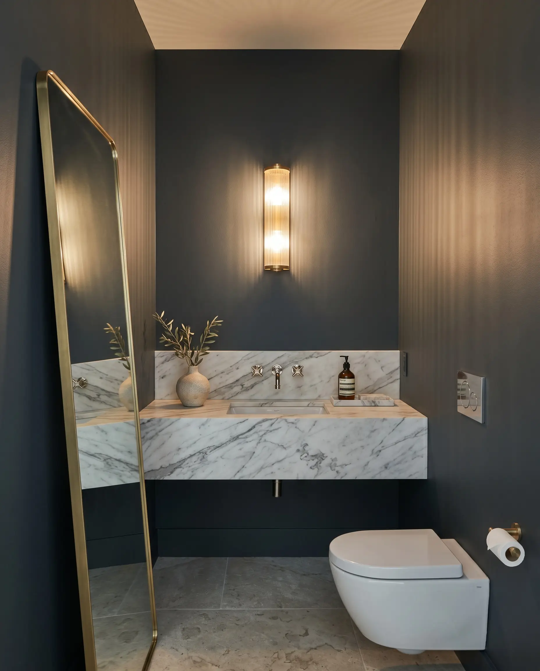 A reeded glass fixture casts textured shadows over a floating statuary marble vanity and polished nickel faucet in a moody low chroma powder room.