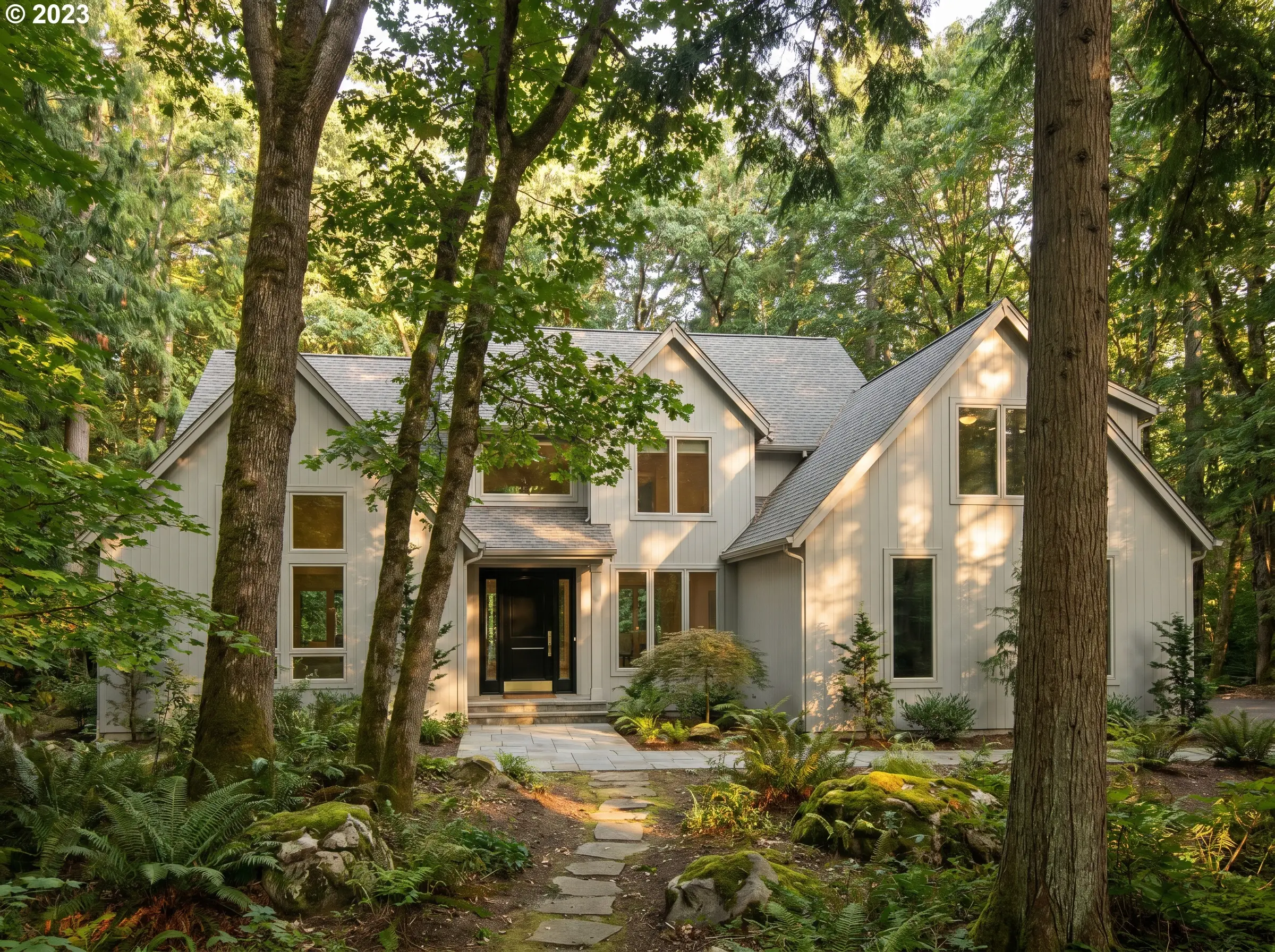 Luminous pale gray exterior house paint covers the siding of a wooded home, contrasting sharply with a glossy black fiberglass front door.