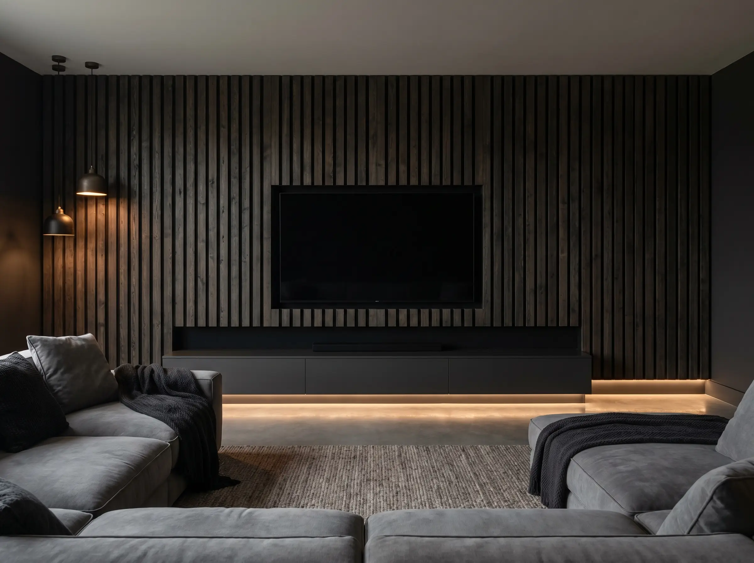 Deeply textured acoustic slat wall panels painted in matte black perfectly camouflage a powered-down television above a dark charcoal media unit and plush grey sectional.