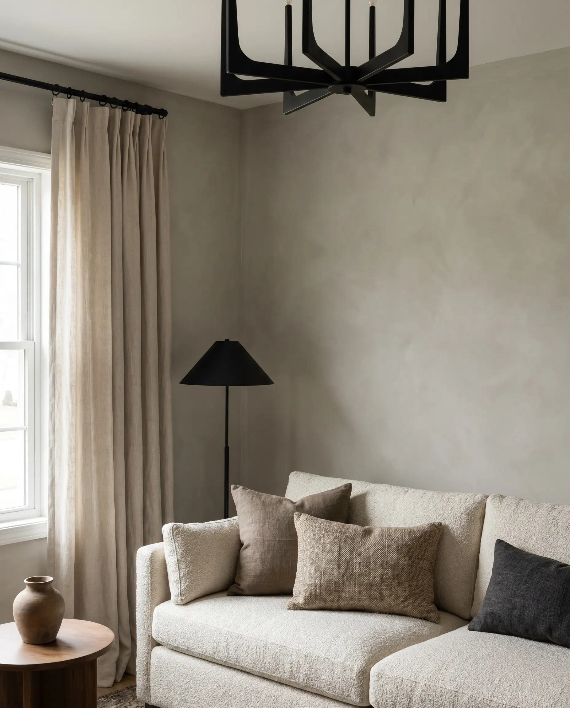 A striking matte black light fixture and matching curtain rod act as sharp visual anchors inside a soft limewash wall living room.