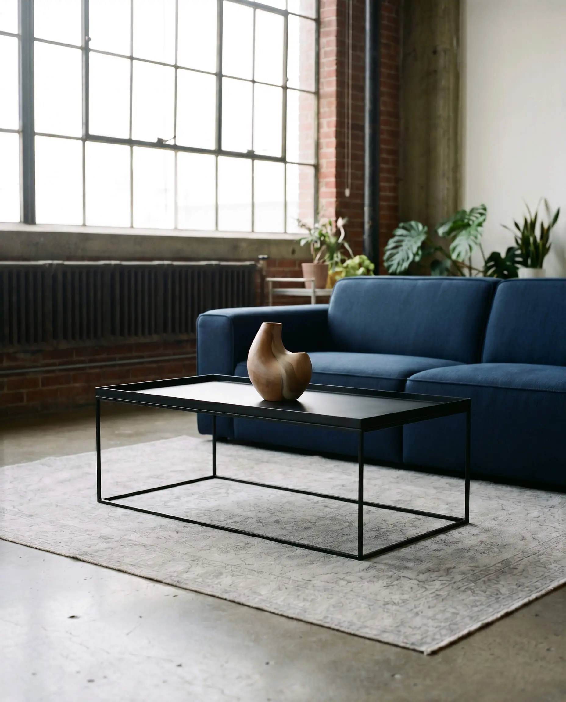 Ultra-thin gauge metal legs support a matte black iron tray table before a structured navy blue sofa and a light gray vintage-faded rug.