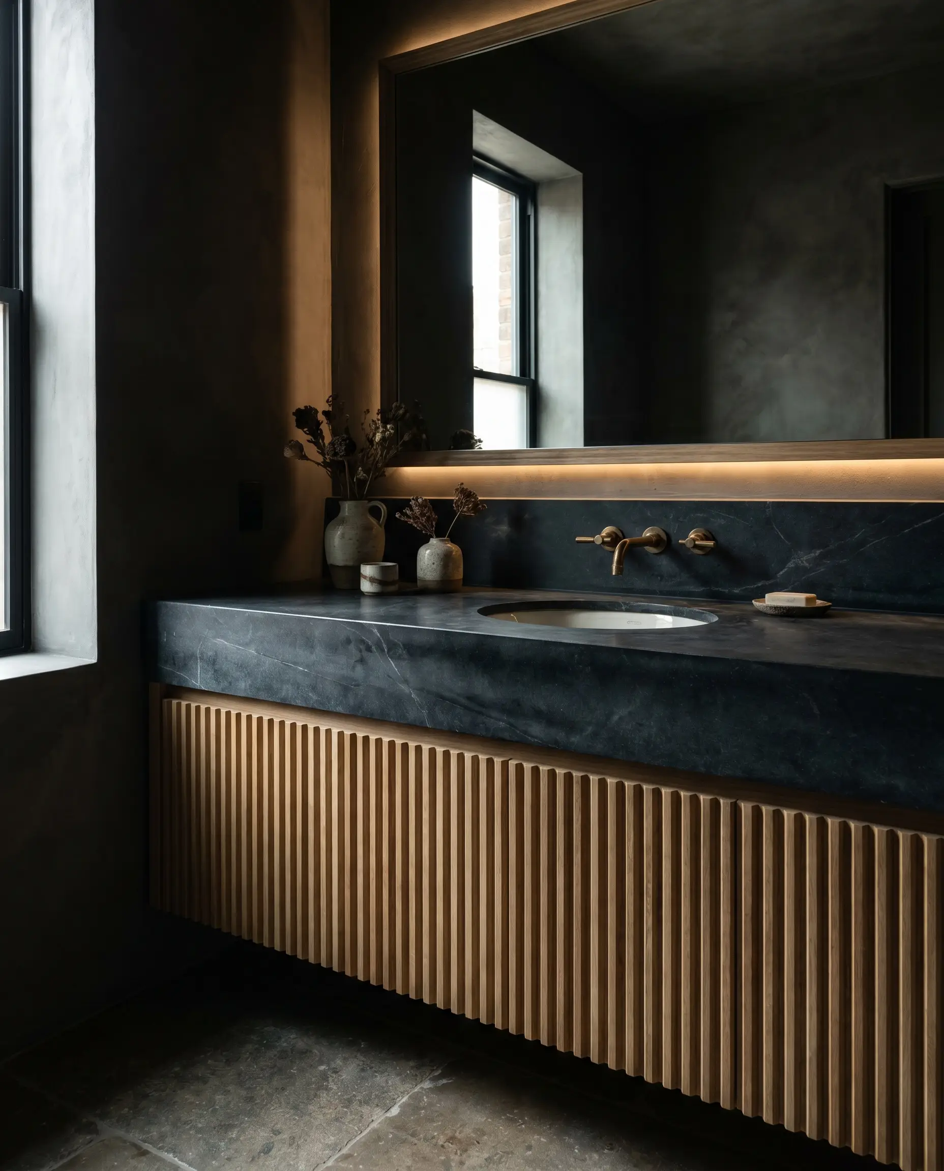 A smooth charcoal matte black soapstone countertop provides high-contrast architectural tension against the light rigid ribbed wood flutes of the cabinet base.