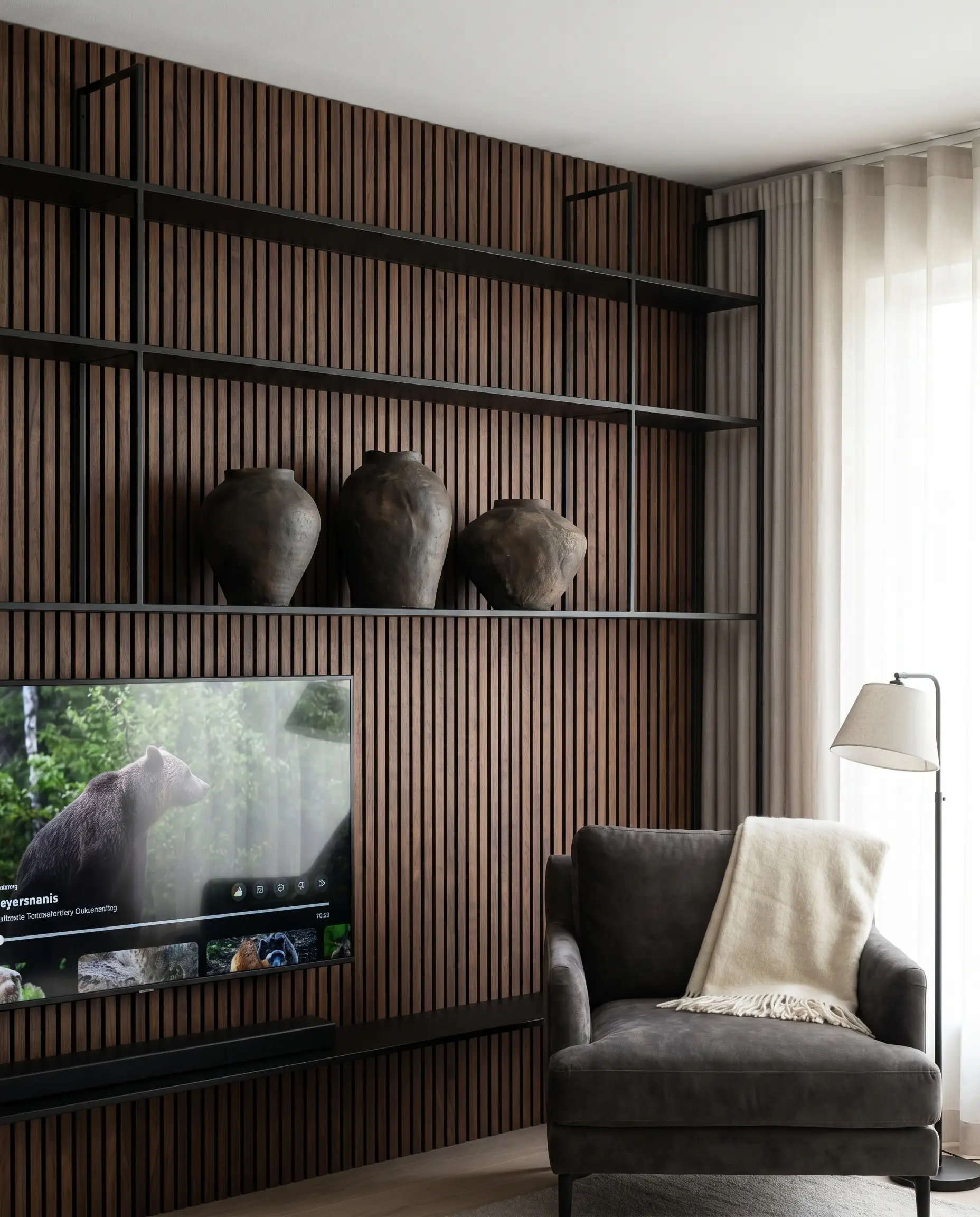 Three oversized dark clay ceramic vessels rest on matte black steel floating shelves integrated directly into a dark wood slat media wall.