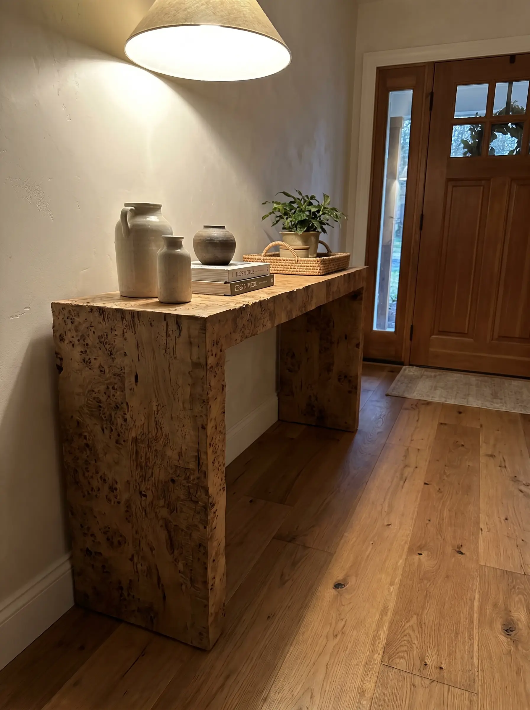 A beautifully crafted modern burl wood foyer table features a matte open-pore wax sealant finish revealing raw tactile ridges alongside understated modern decor.