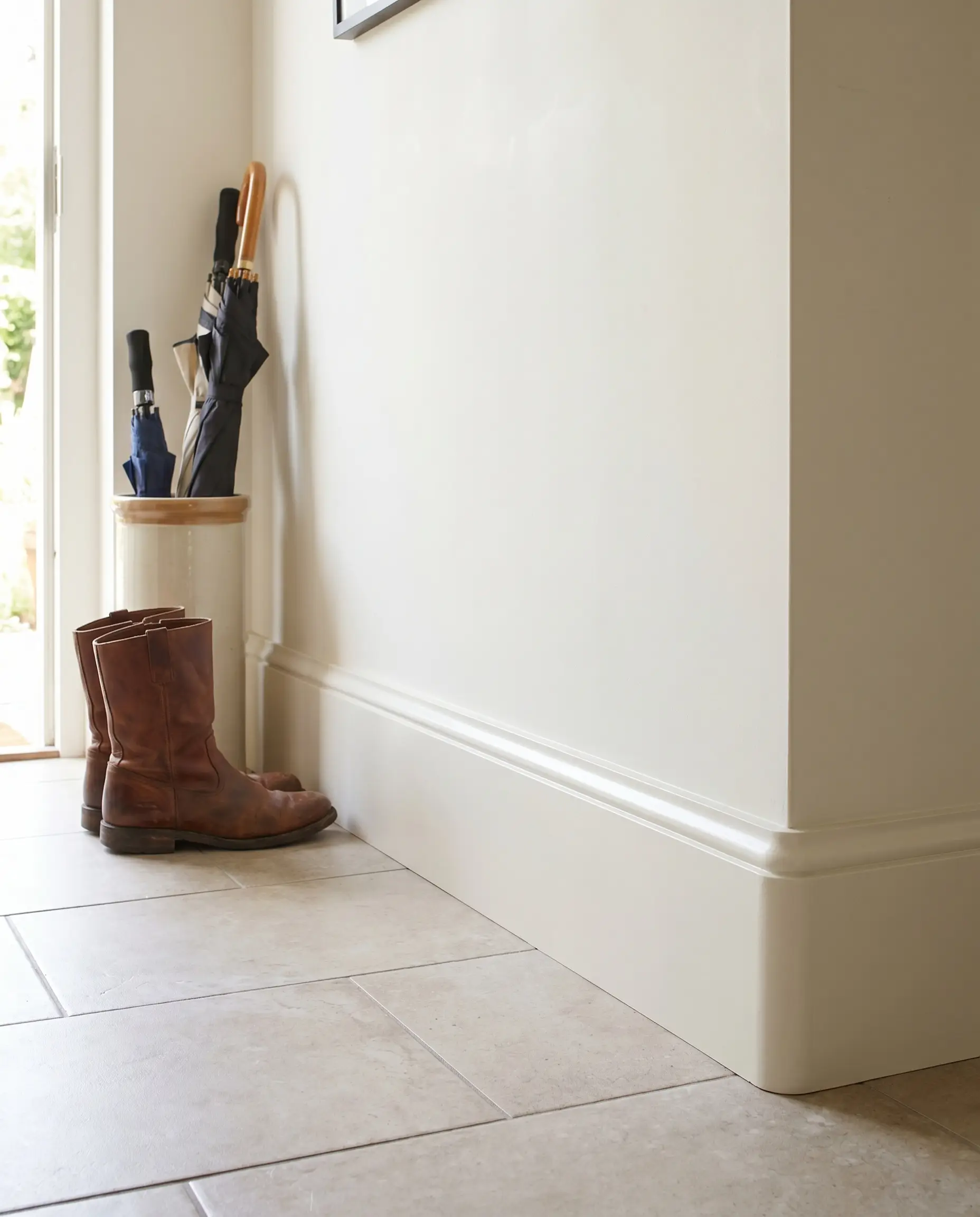 Custom-milled hardwood flat stock trim with a micro-bevel edge seamlessly blends into Pure White walls above a durable ceramic tile entryway floor.