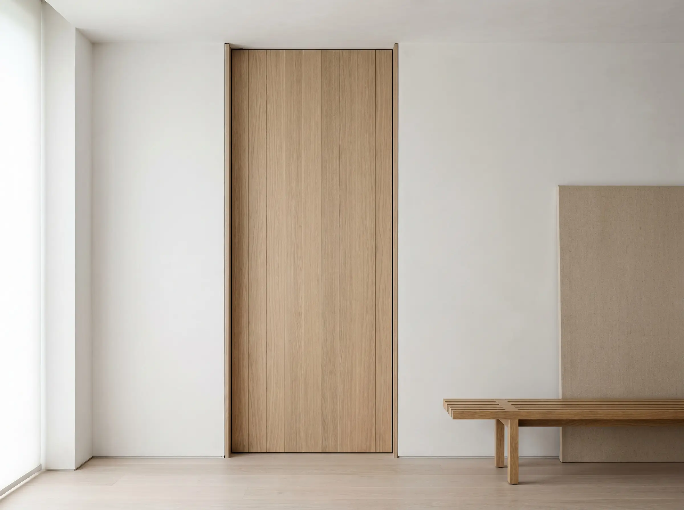 A flush kerfed door jamb with tear-away L-bead drywall finish meets a solid-core pivot door, light ash wood flooring, and a minimalist oak bench.
