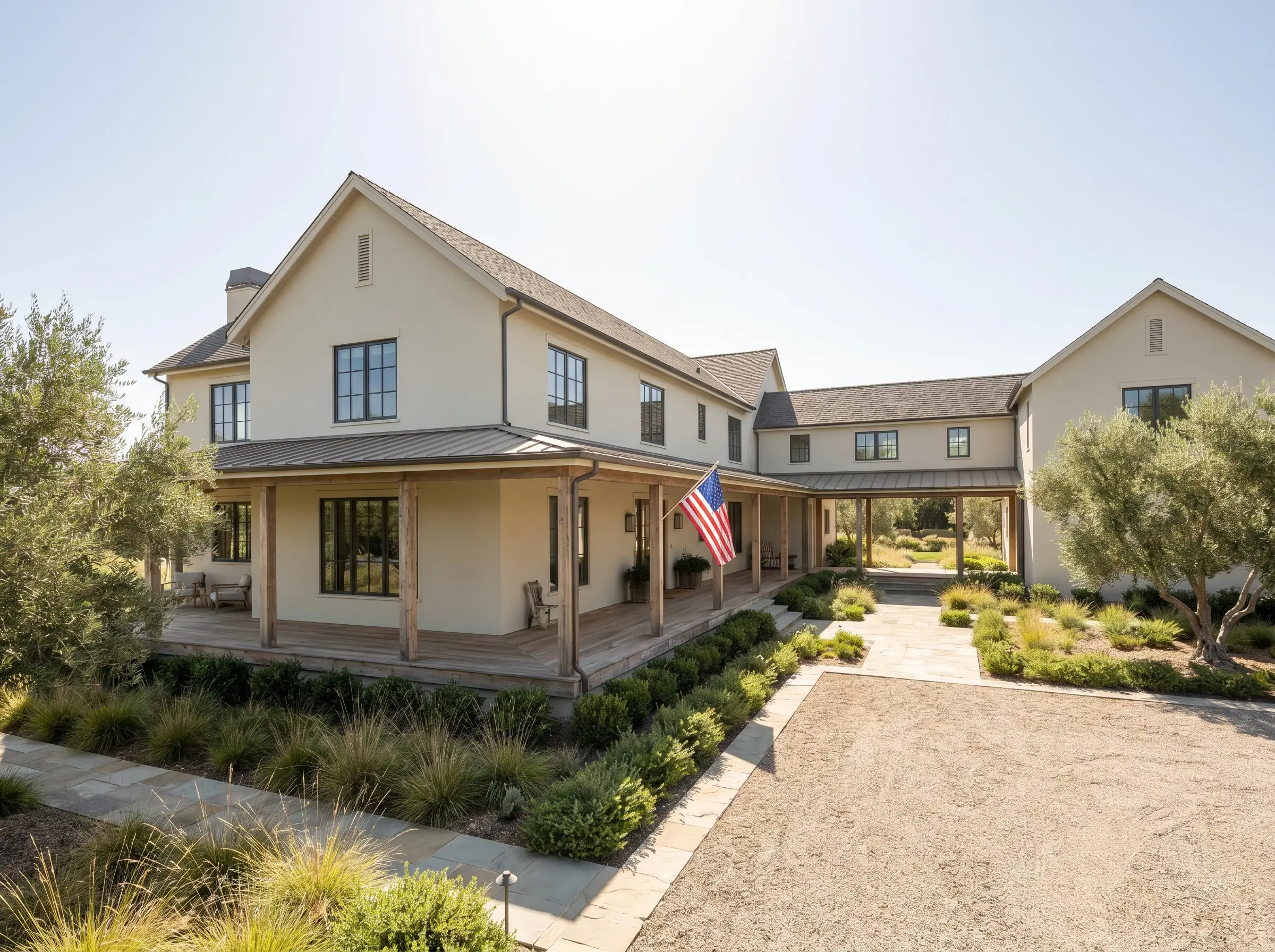 An expansive wrap-around porch and natural wood decking frame a custom build facade painted in grounded Benjamin Moore modern farmhouse exterior colors.