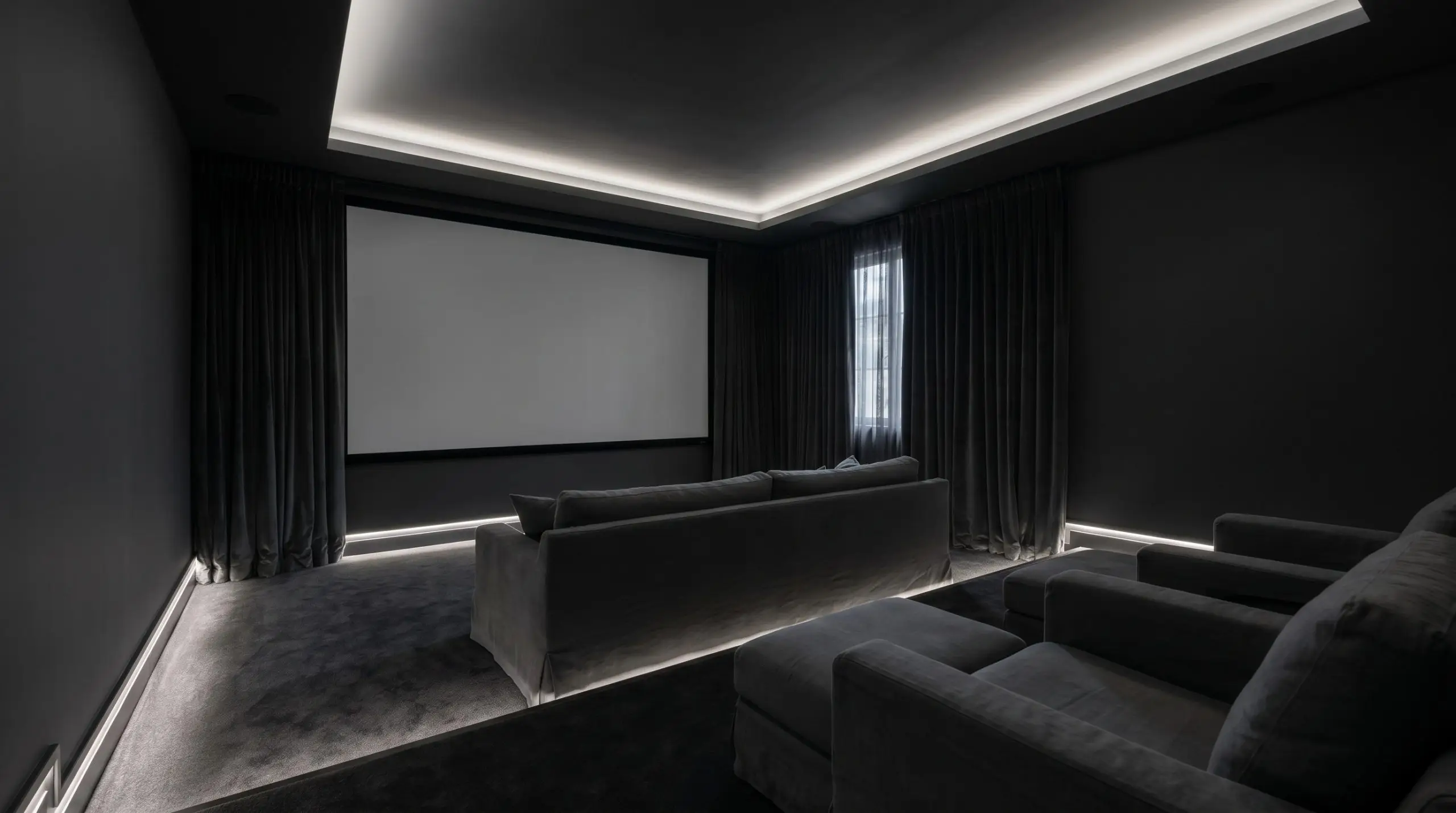 Low-profile slipcovered seating faces a large blank media wall inside a dedicated home theater enveloped entirely in light-absorbing pure charcoal paint.