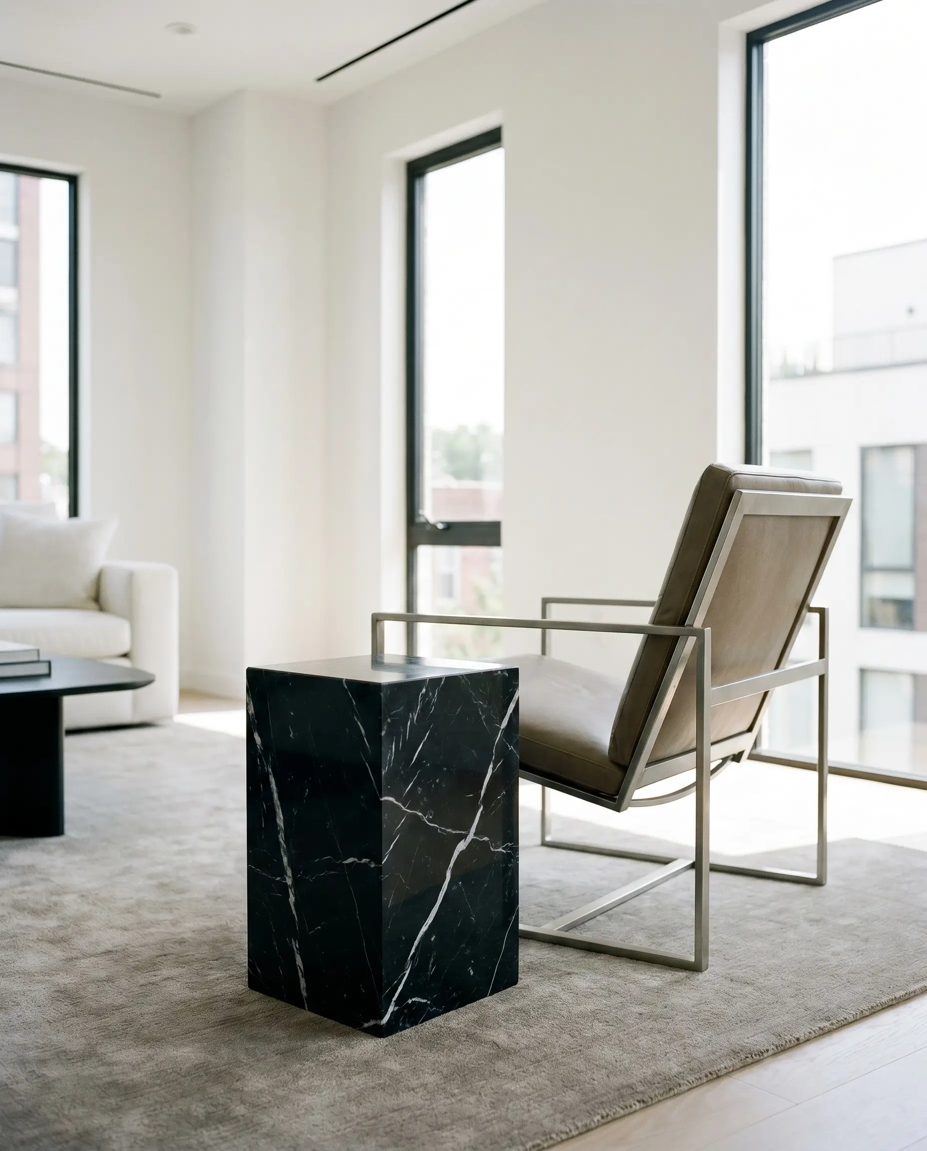 A solid Nero Marquina marble drink table with stark white veining stands next to a lightweight metal-framed modern lounge chair on a tonal rug.