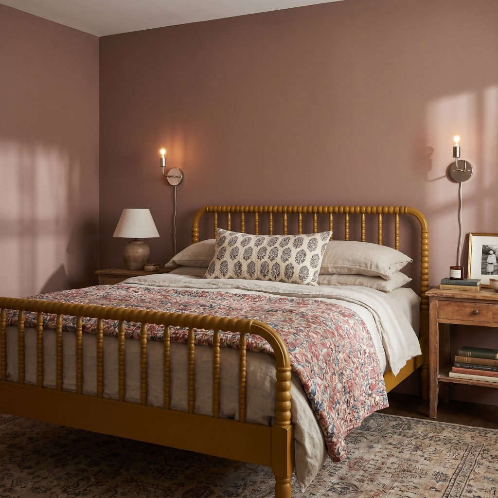 A deep mustard spindle bed dressed in oatmeal washed linen and a floral chintz quilt rests between polished nickel sconces in a vintage-inspired bedroom.