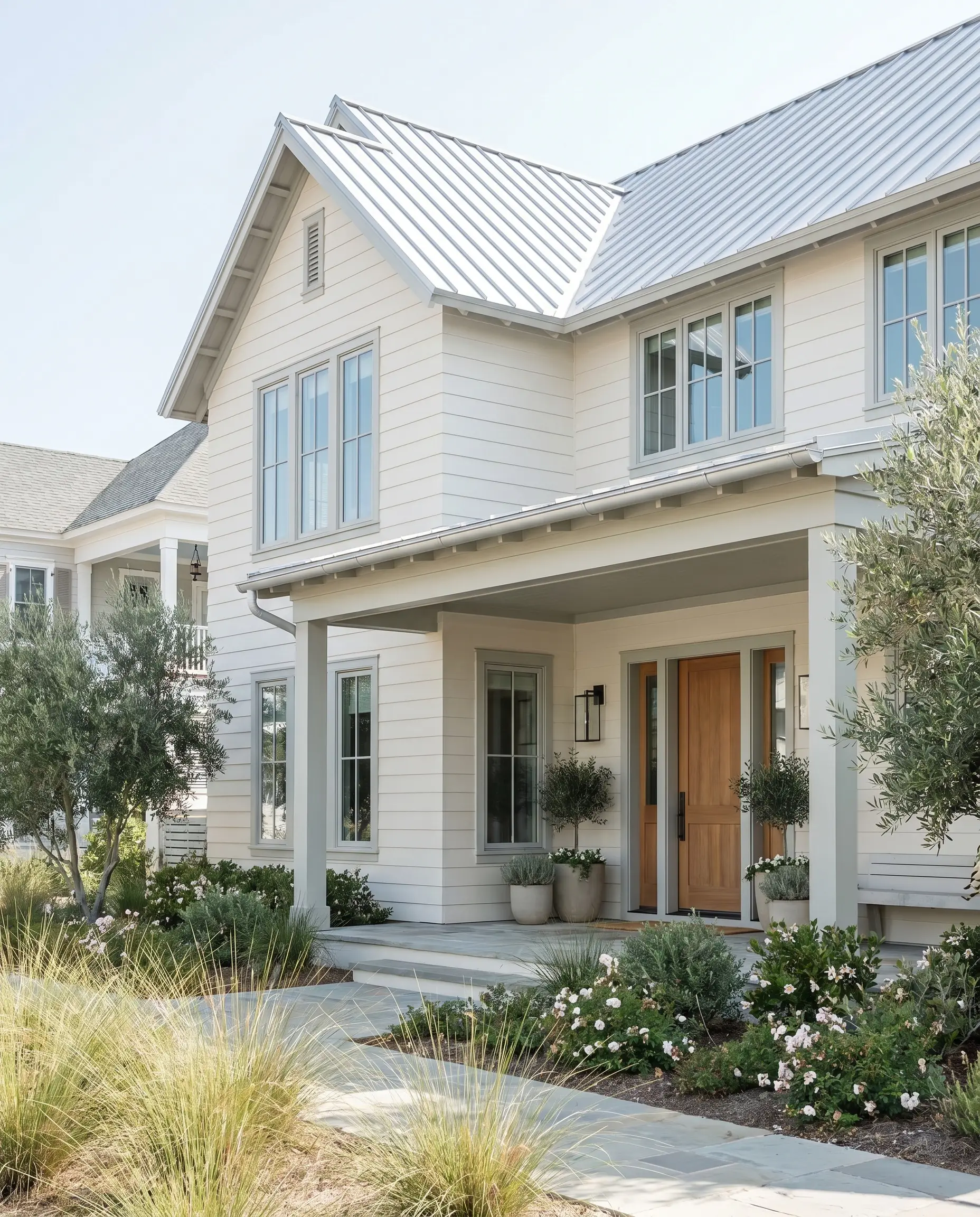 Off-white exterior siding is accented by pale gray trim and a sleek silver-toned metal roof on a coastal contemporary home.