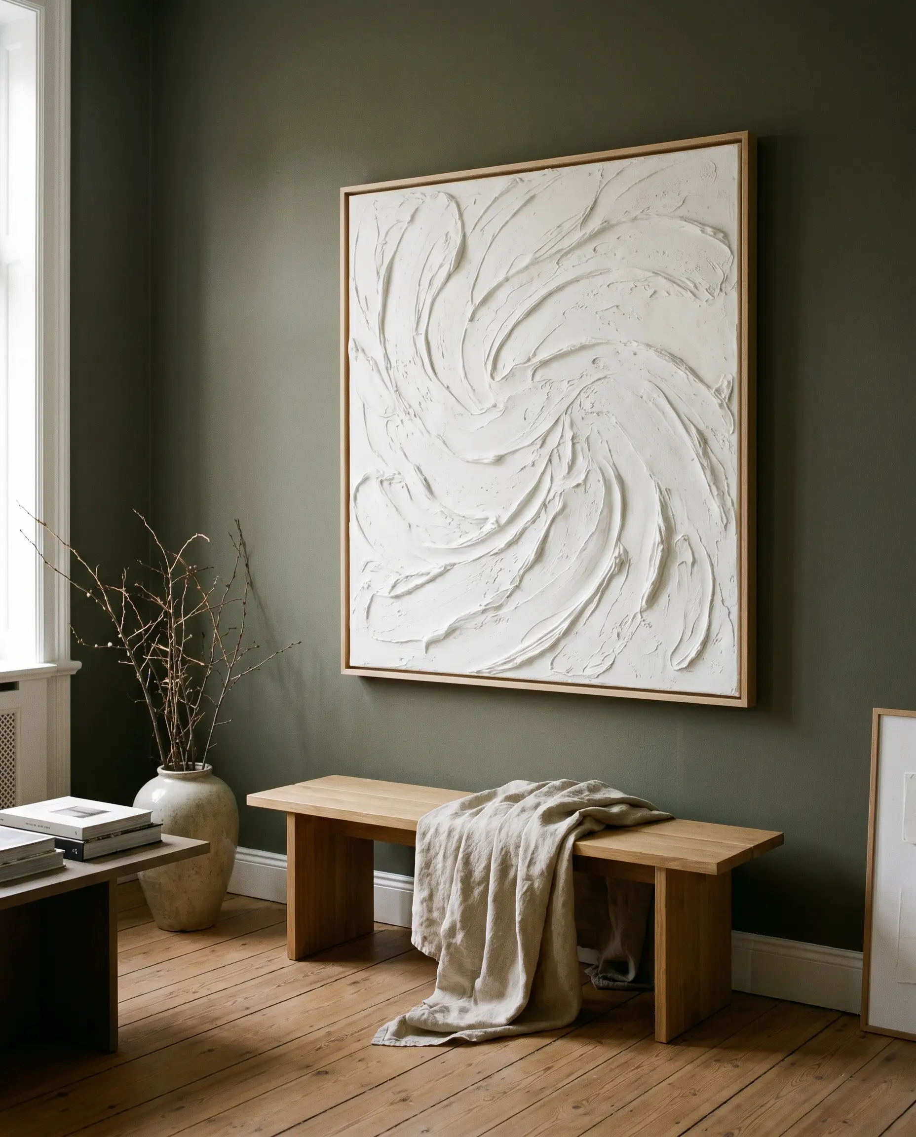 An oversized textured white plaster canvas art piece in a light wood float frame hangs above a contemporary bench and linen throw.