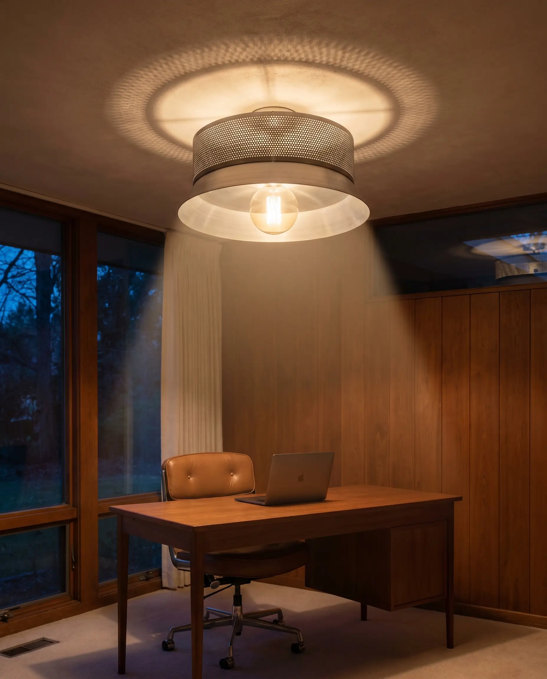 A shallow spun aluminum metal shade with tiny perforations casts a downward beam over a home office featuring a sleek teak desk and leather task chair.