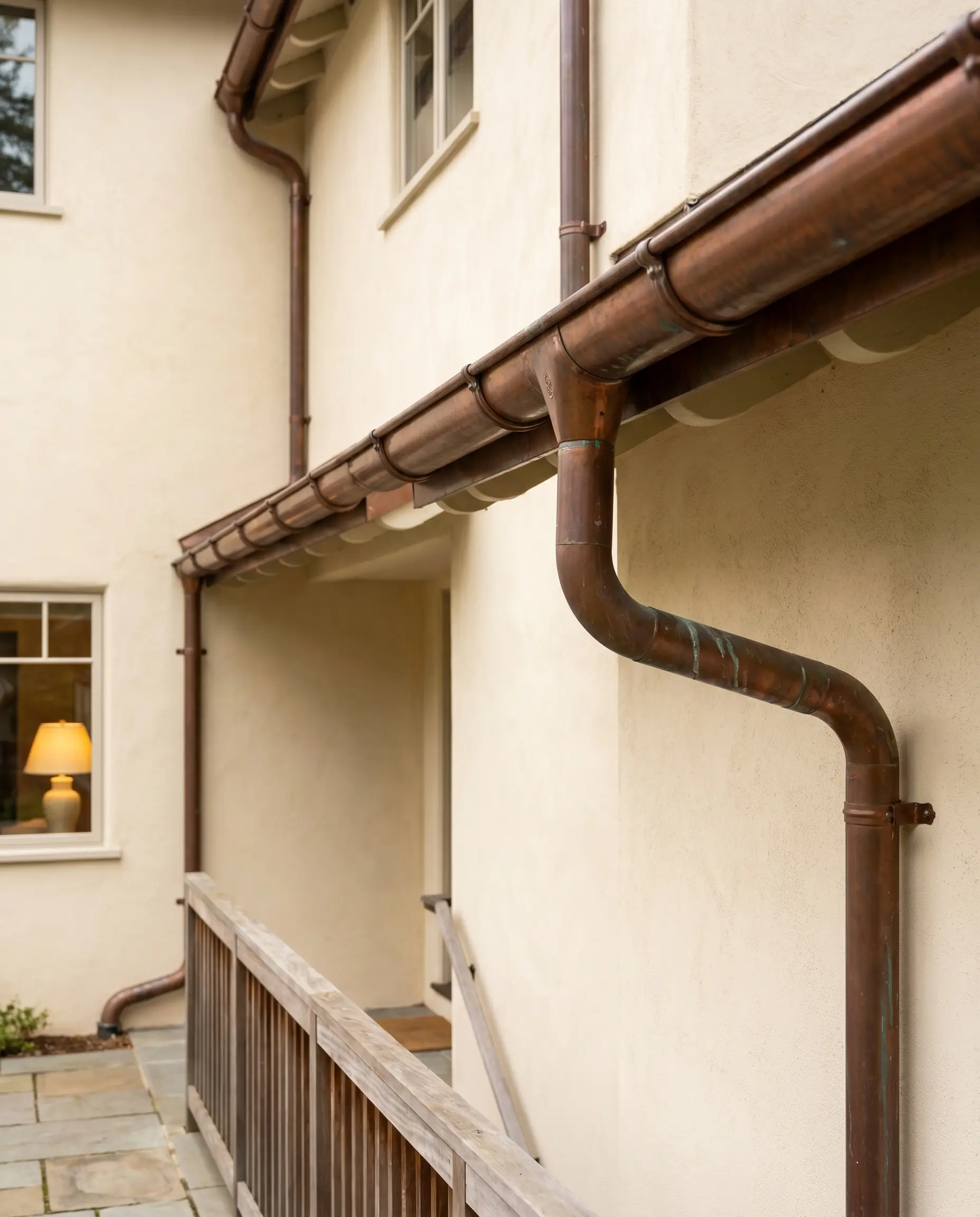 Half-round copper gutters and downspouts displaying a rich penny-brown patina accent a smooth Pointing warm cream exterior wall.