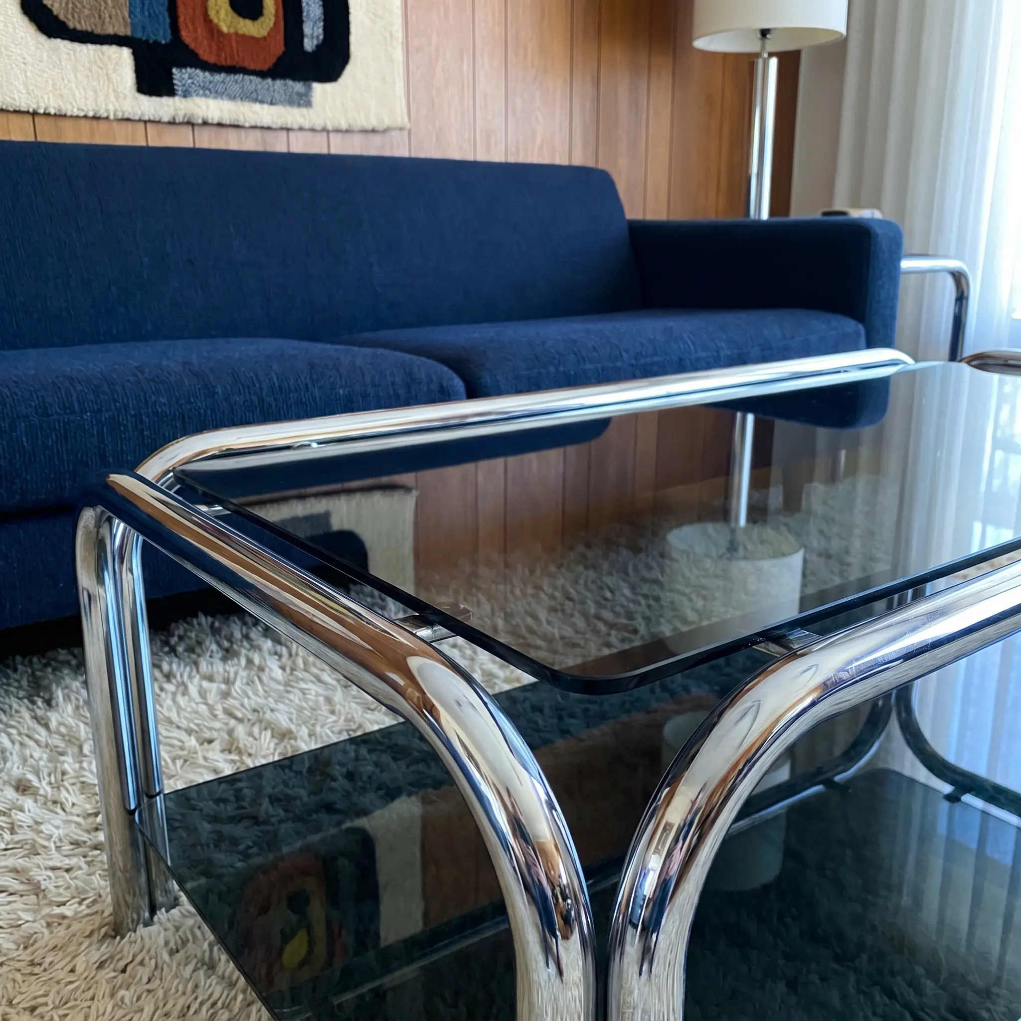 Tubular polished chrome frames and smoked glass form striking coffee tables to match a navy blue sofa in this retro-modern 1970s revival living room.