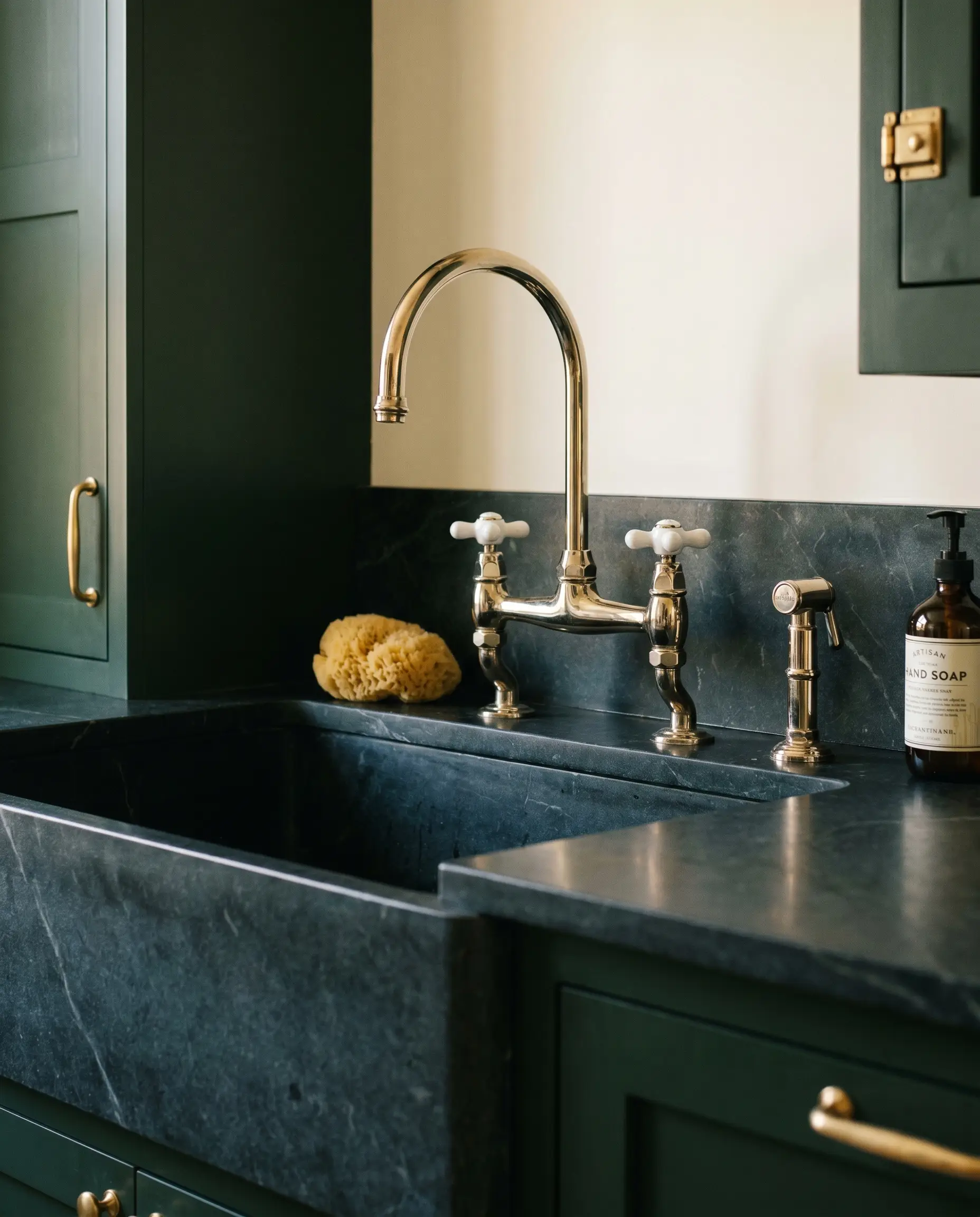 A classic polished nickel bridge faucet with porcelain cross handles arches over a deep sink surrounded by Benjamin Moore Essex Green cabinetry and charcoal stone.