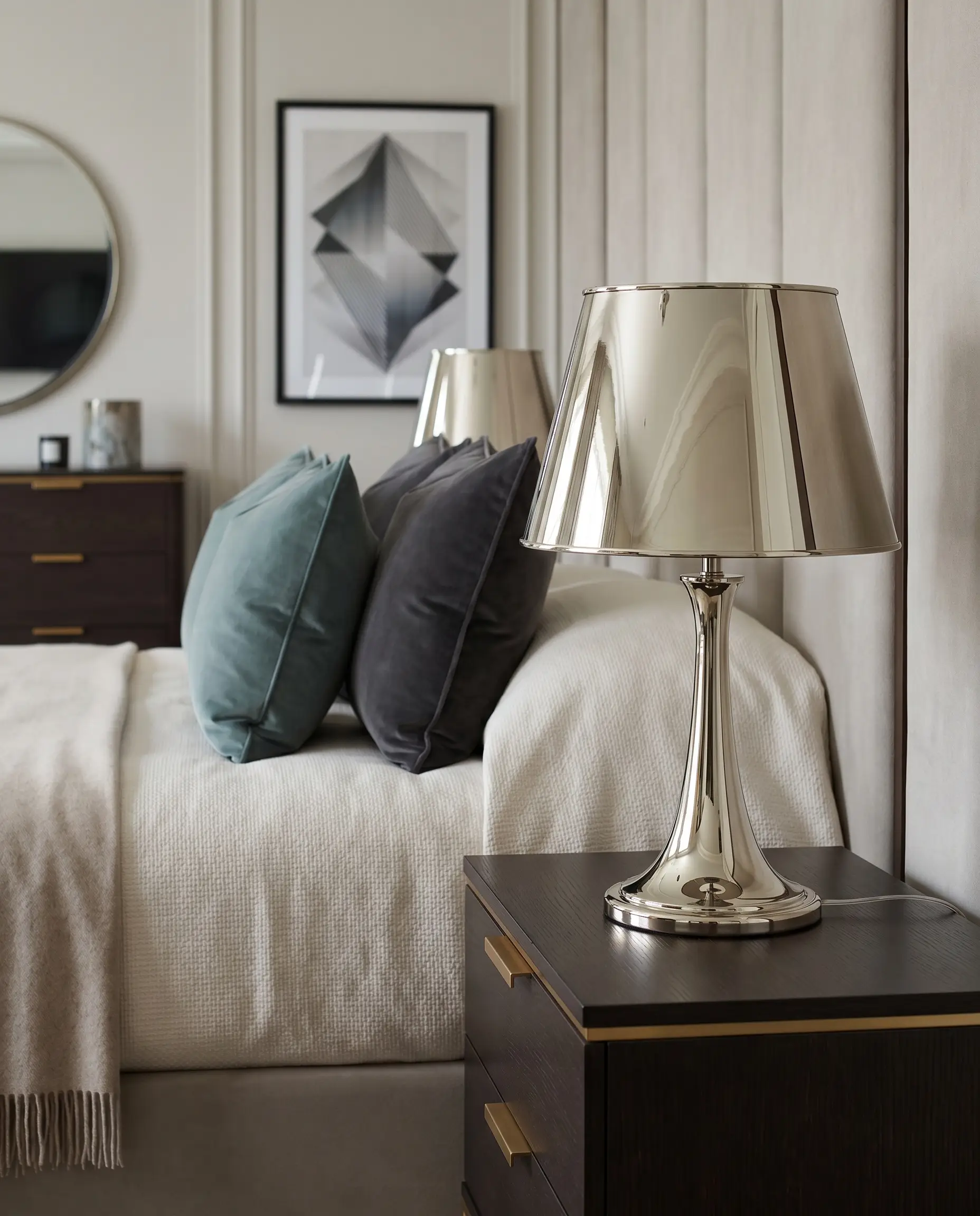 A polished nickel table lamp sits on a sleek nightstand fitted with warm unlacquered brass hardware beside a bed dressed in matte fabrics.