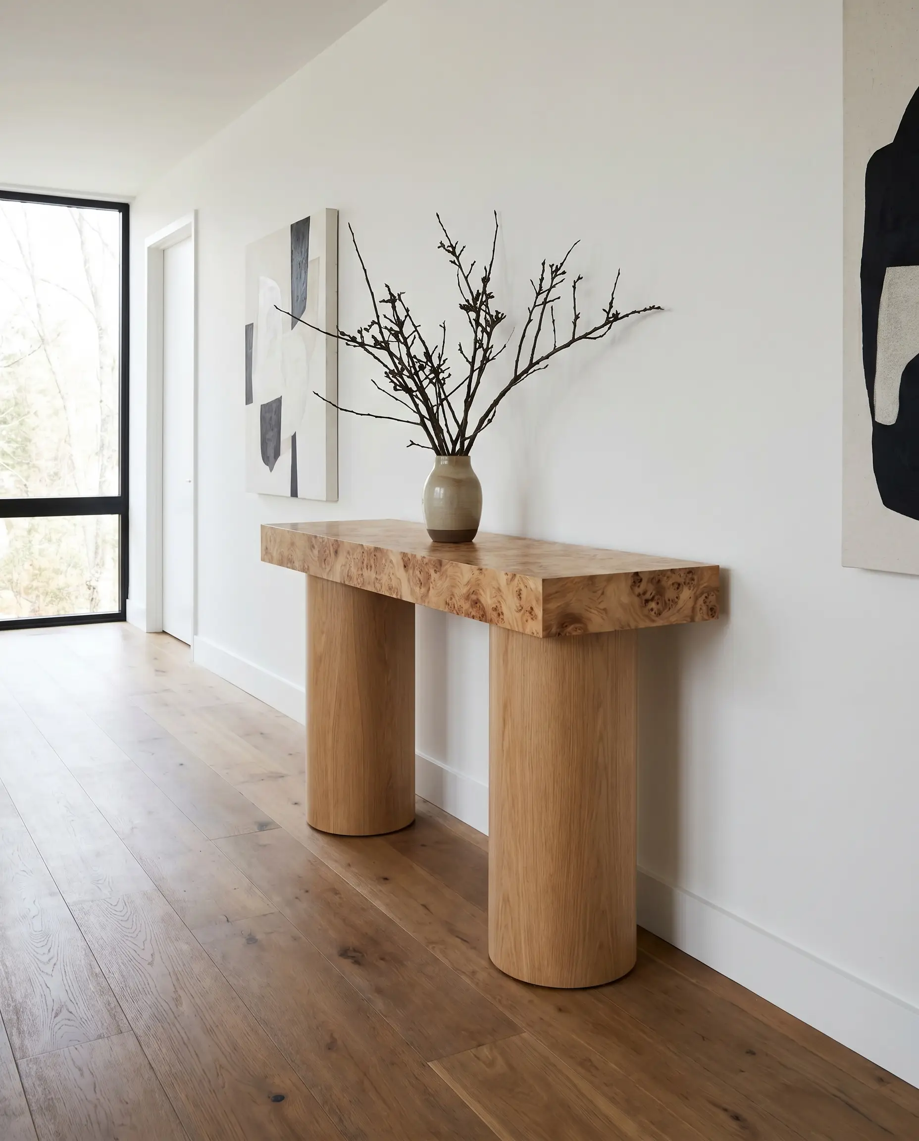 A postmodern Mappa burl console table rests on dual oversized cylindrical armatures, displaying a minimal structural branch arrangement against crisp white gallery walls.