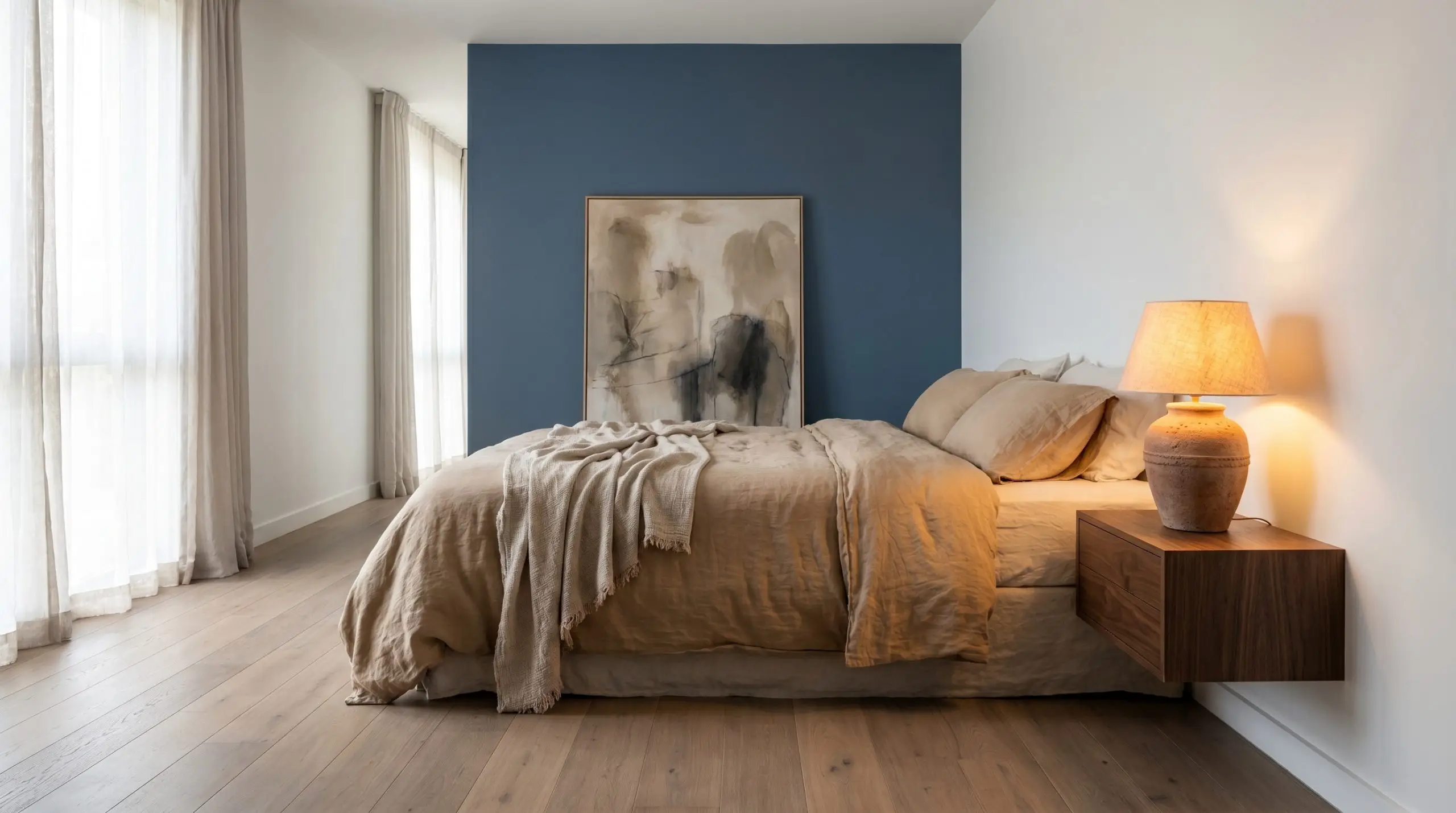 A striking accent wall painted in Benjamin Moore Van Deusen Blue (Hex #485B6E) creates a moody backdrop for washed linen bedding, an abstract canvas, and a vintage terracotta lamp.