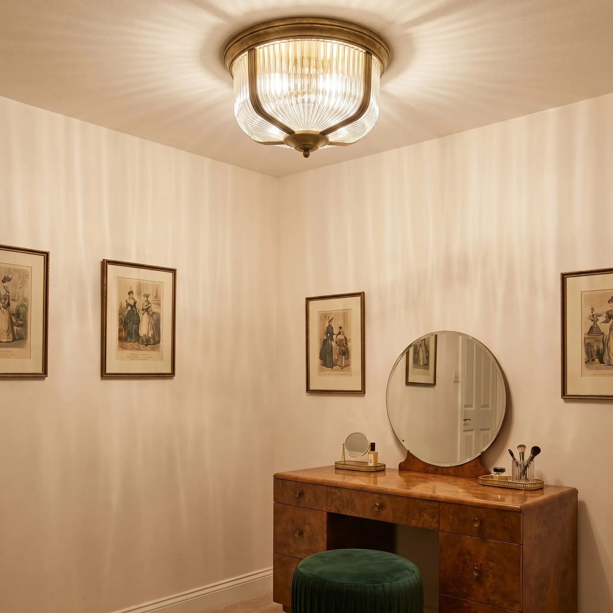 A heavy cast ribbed glass semi-flush mount with vertical fluting casts elongated shadows over a vanity setup featuring a burled wood desk and velvet stool.