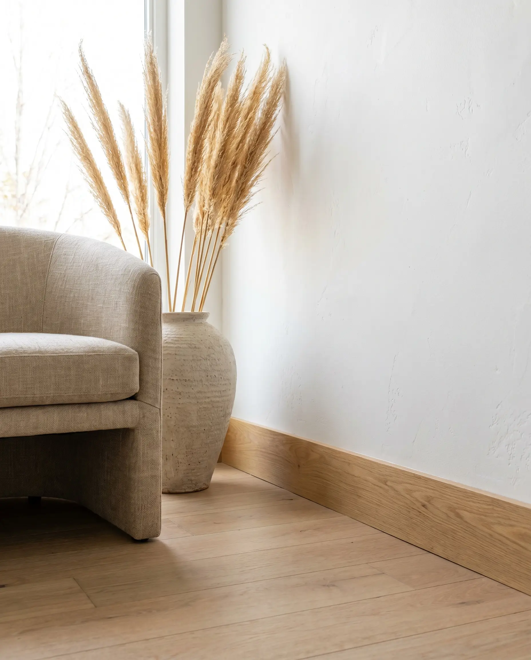 Solid natural rift-sawn white oak flat stock millwork borders a stark white wall alongside a raw linen accent chair and ceramic floor planter.