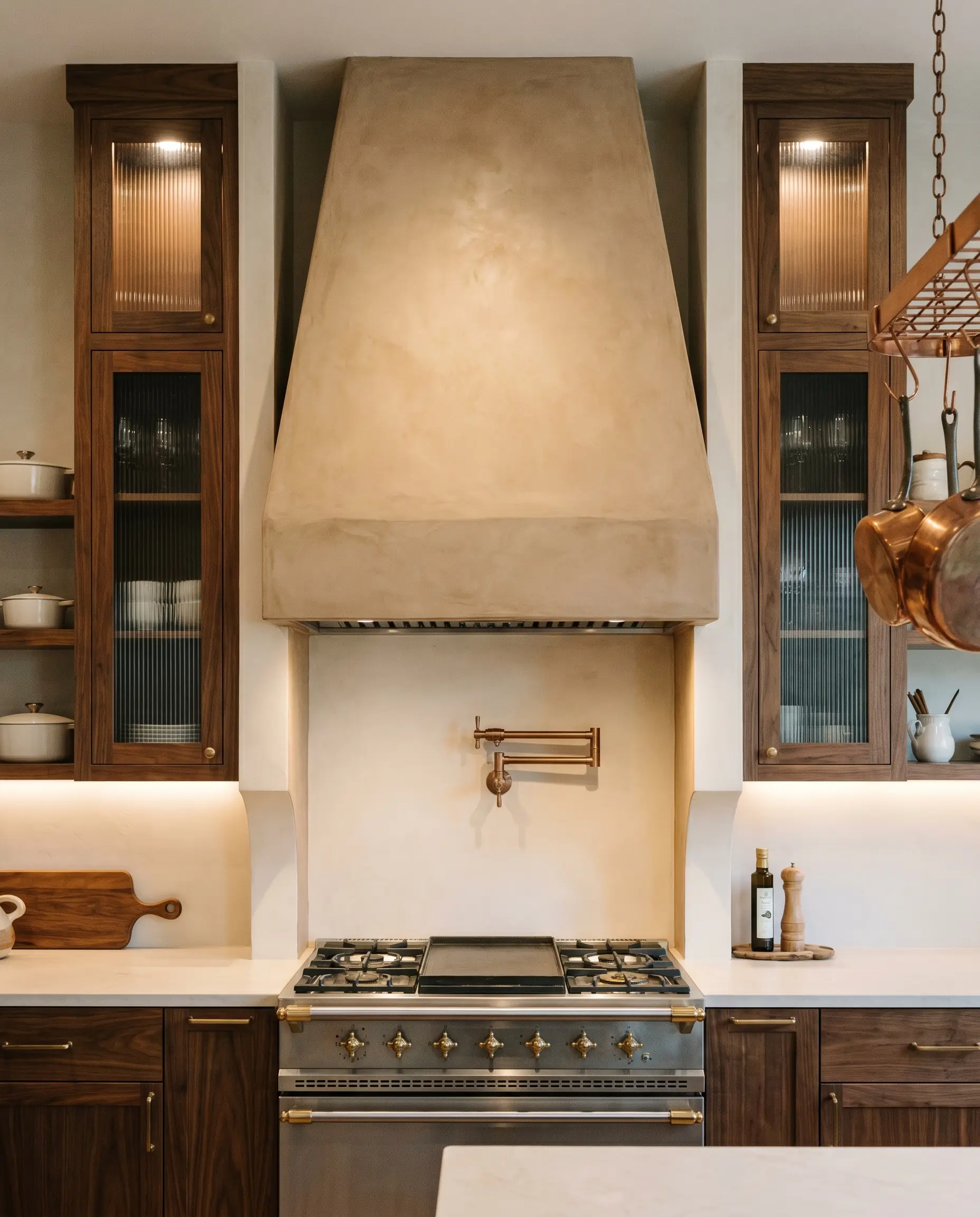 Custom walnut framed fluted glass upper cabinets and rift-sawn base units flank a hand-troweled Roman clay range hood and stainless stove.