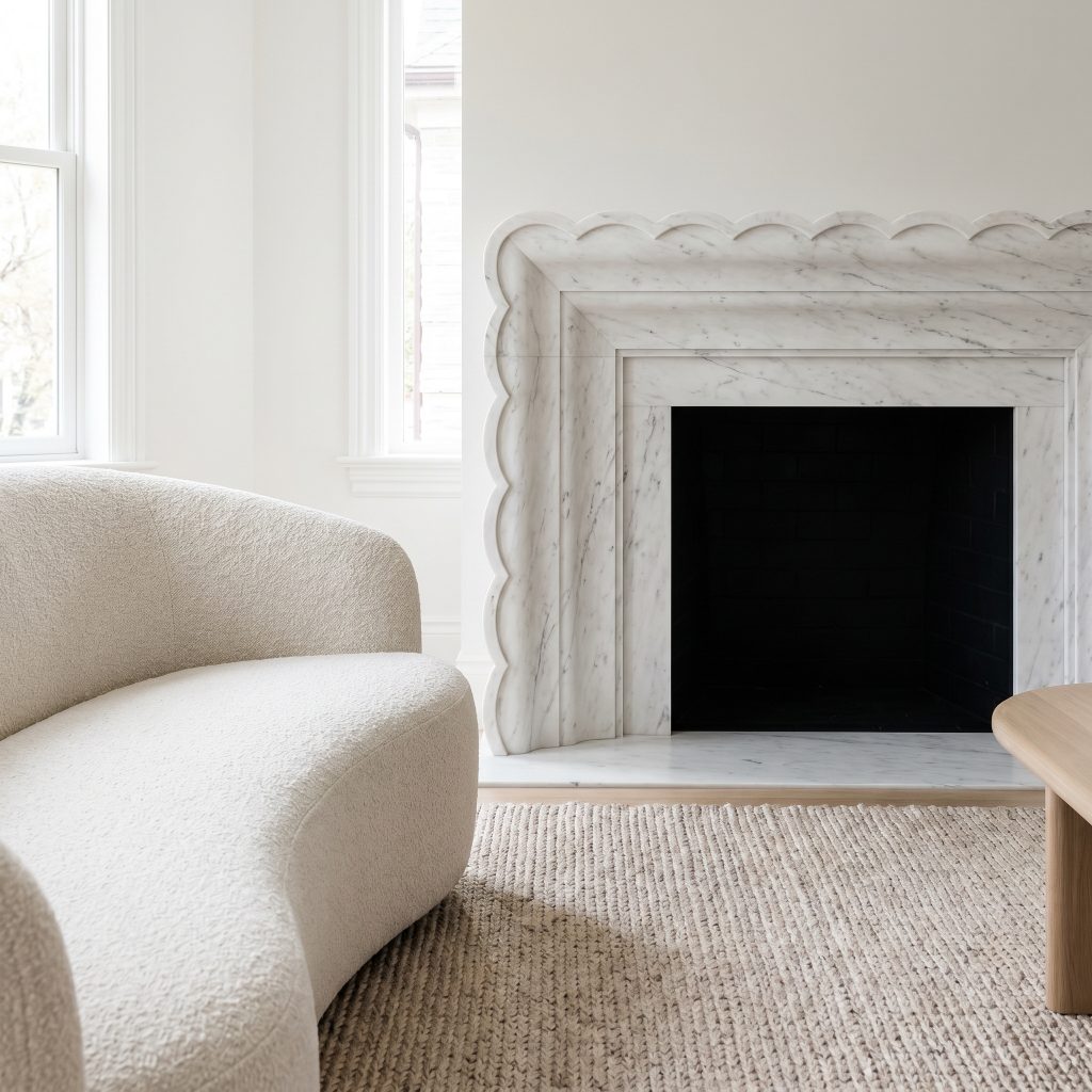 A fine-grained Danby stone mantel features a custom-milled scalloped edge profile overlooking a curved bouclé sofa and a subtle woven rug.