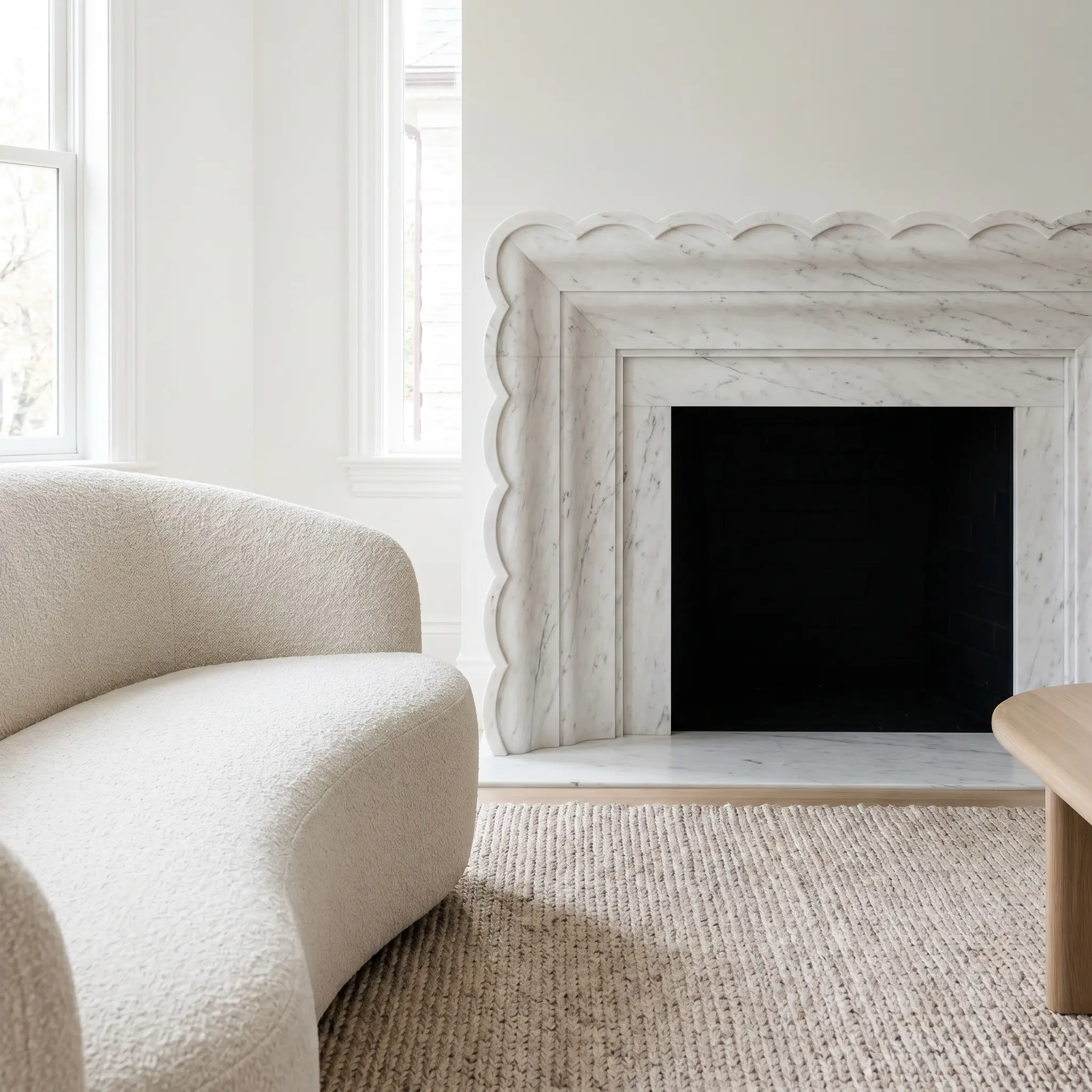 A fine-grained Danby stone mantel features a custom-milled scalloped edge profile overlooking a curved bouclé sofa and a subtle woven rug.