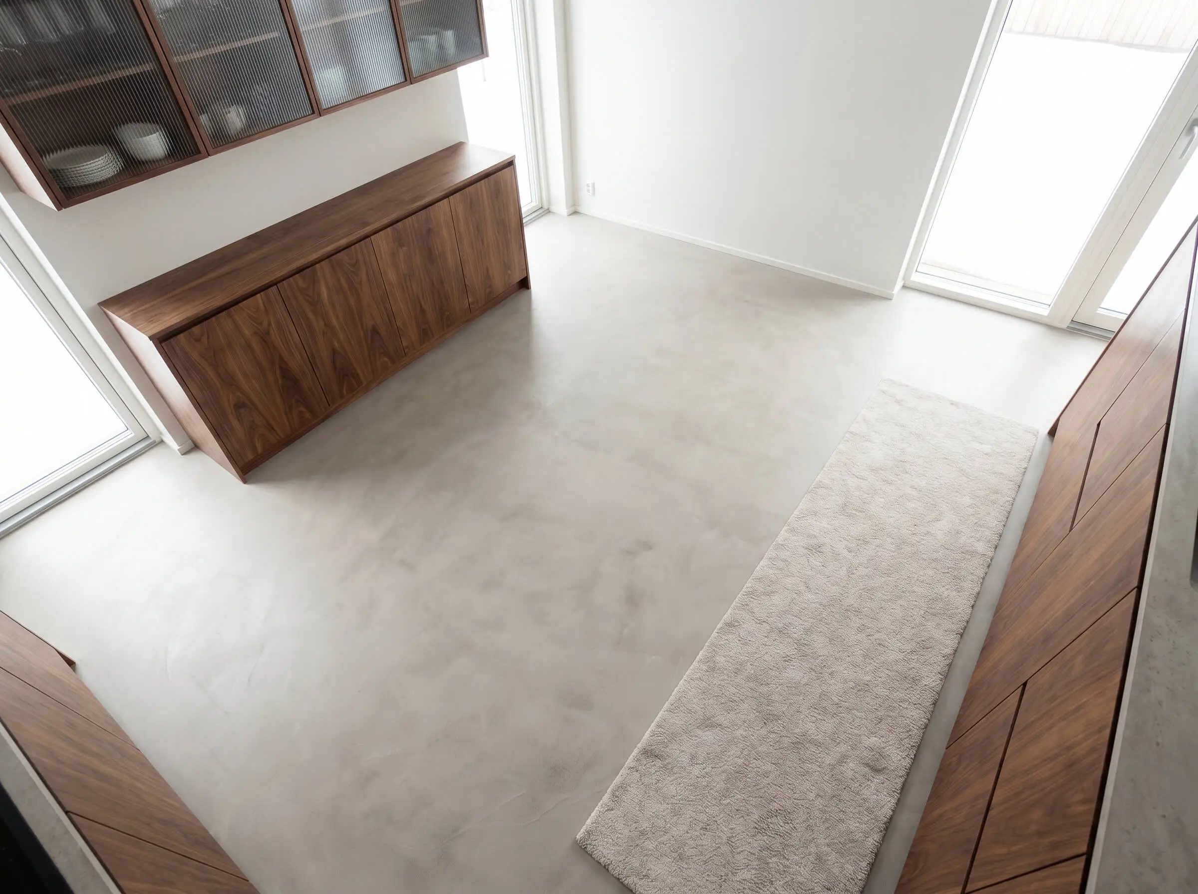 A seamless greige microcement floor and a neutral textured runner rug anchor flat-slab wood base units and ribbed glass upper cabinets.