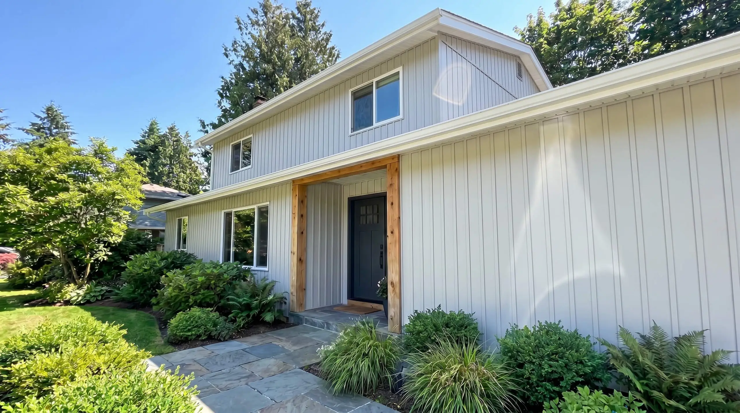 Sleek vertical paneling siding painted in Sherwin-Williams Reflection (Hex #D3D5D3) contrasts against crisp white fascia boards, rough-hewn cedar columns, and a natural slate walkway.