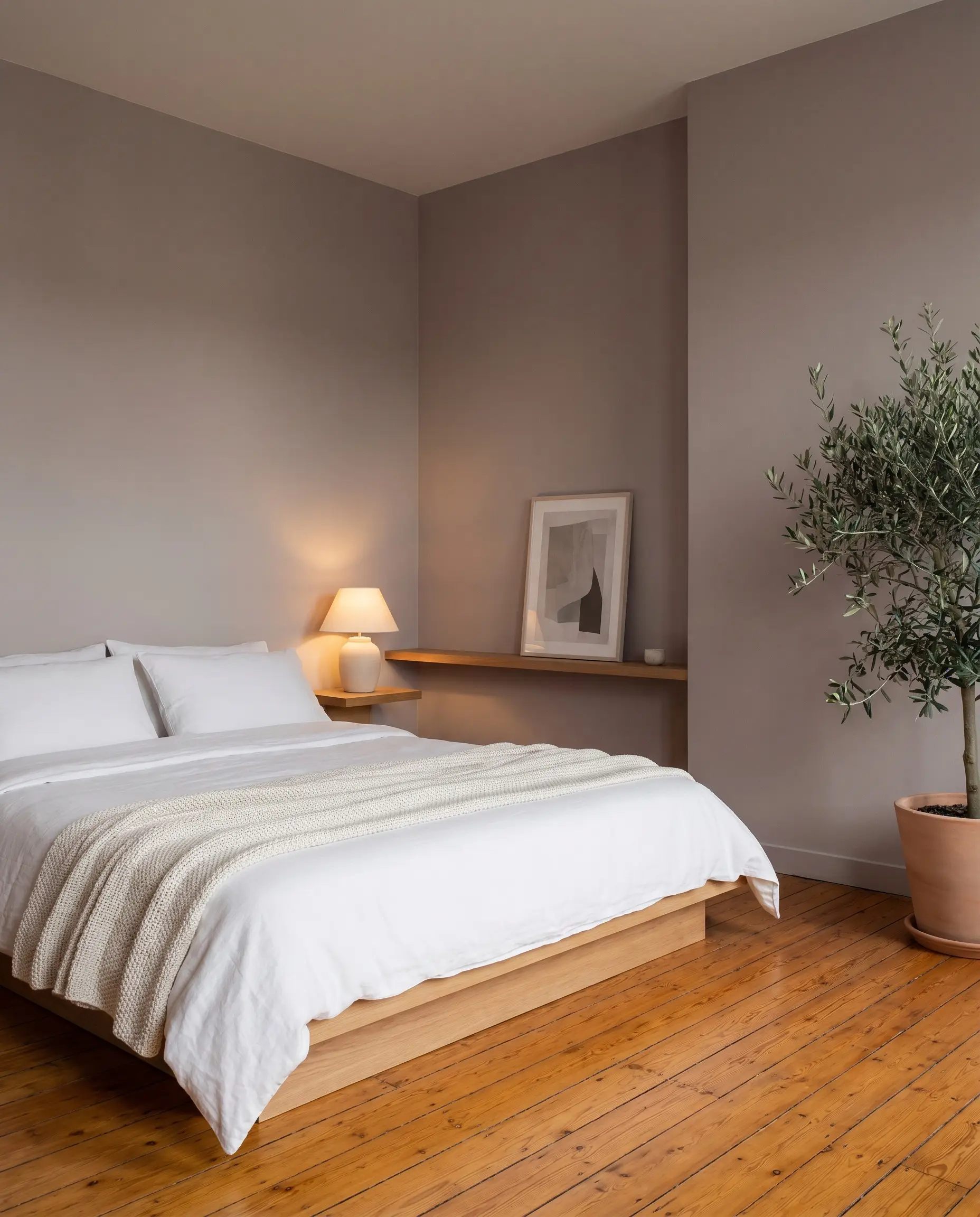 A minimalist platform bed dressed in tailored white bedding sits on ambered legacy oak floors surrounded by Farrow & Ball Skimming Stone walls.