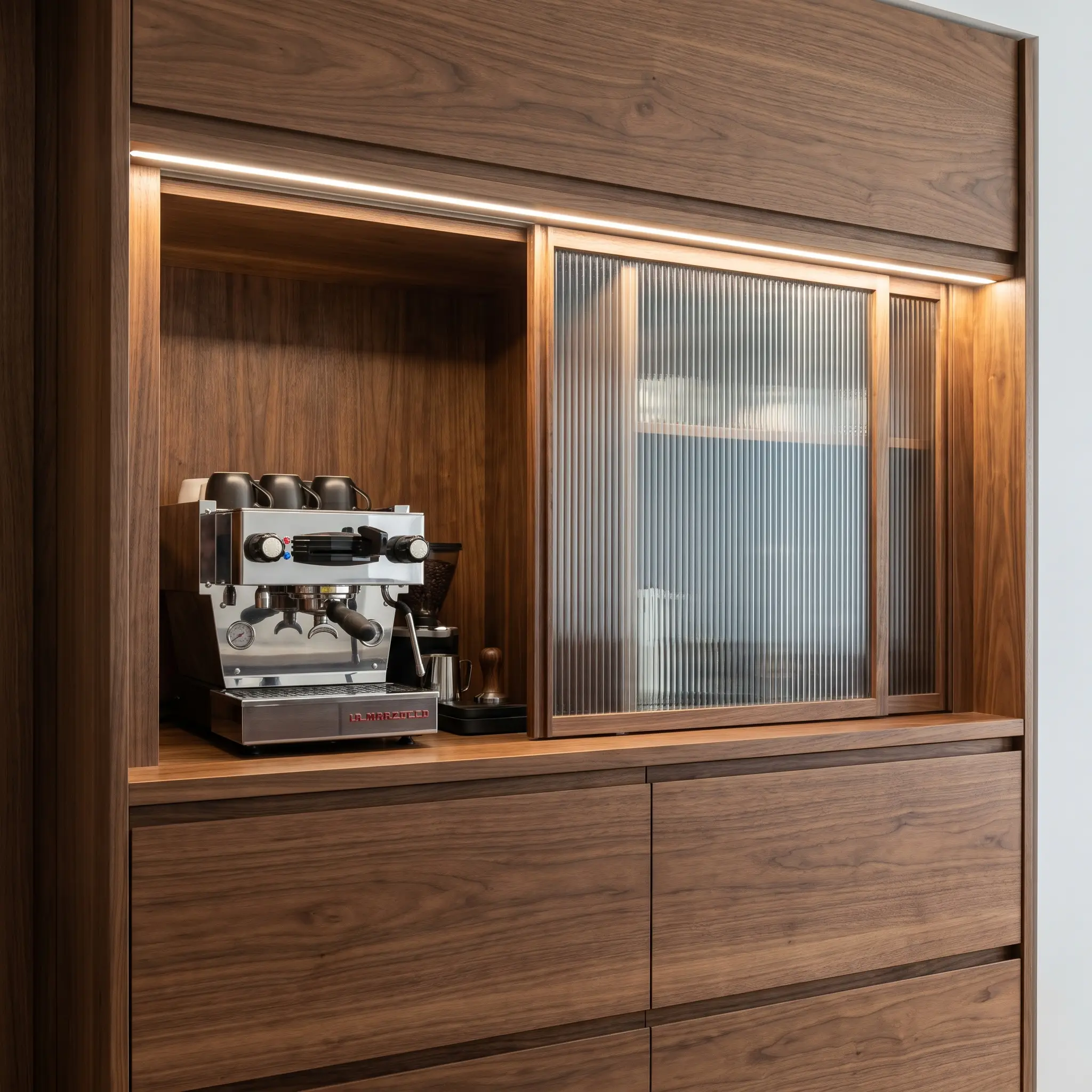 Sliding reeded glass and walnut kitchen cabinet fronts conceal a high-end appliance garage lined with matching wood veneer above flat-slab bases.