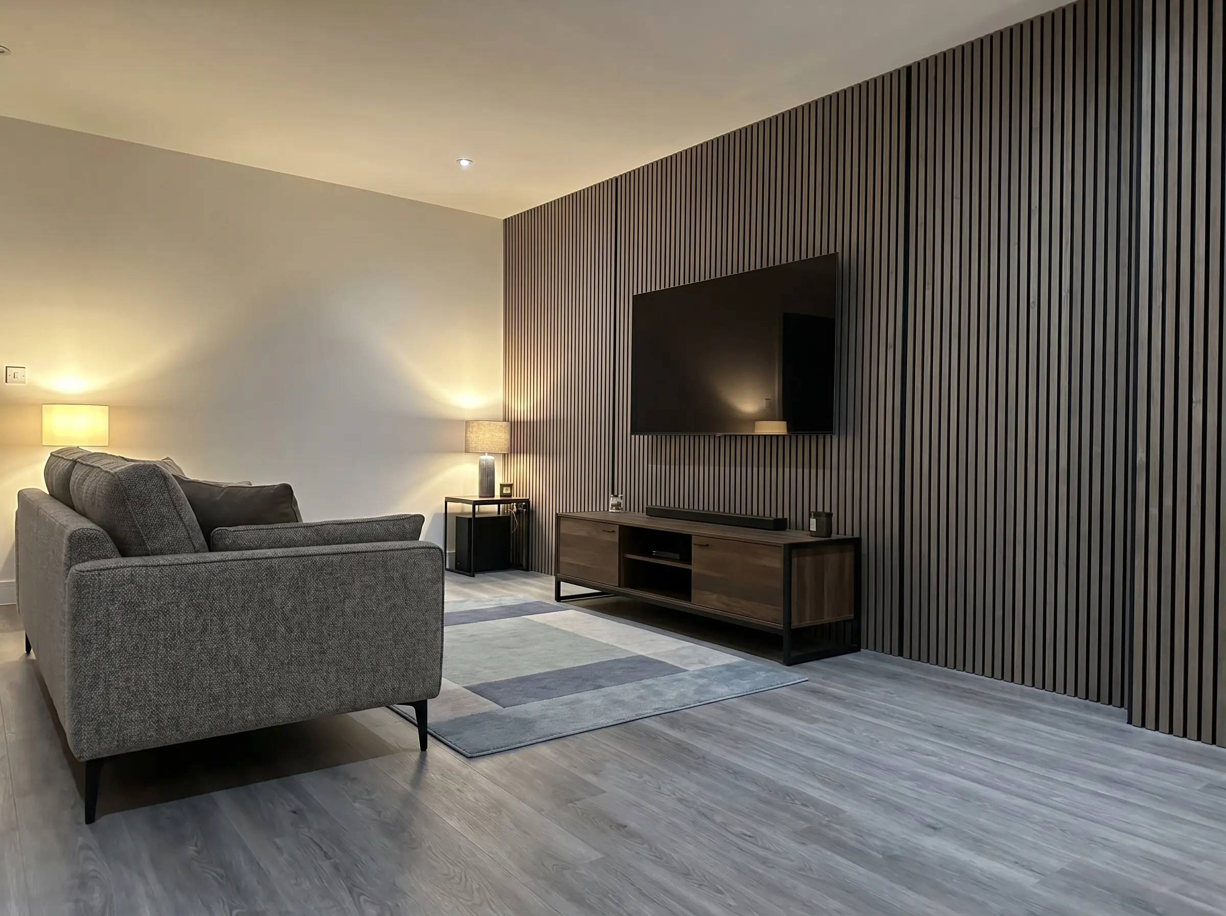 Cool-toned Smoked Larch acoustic wood slats perfectly communicate with the grey undertones of luxury vinyl plank flooring in this wood slat tv wall modern living room.